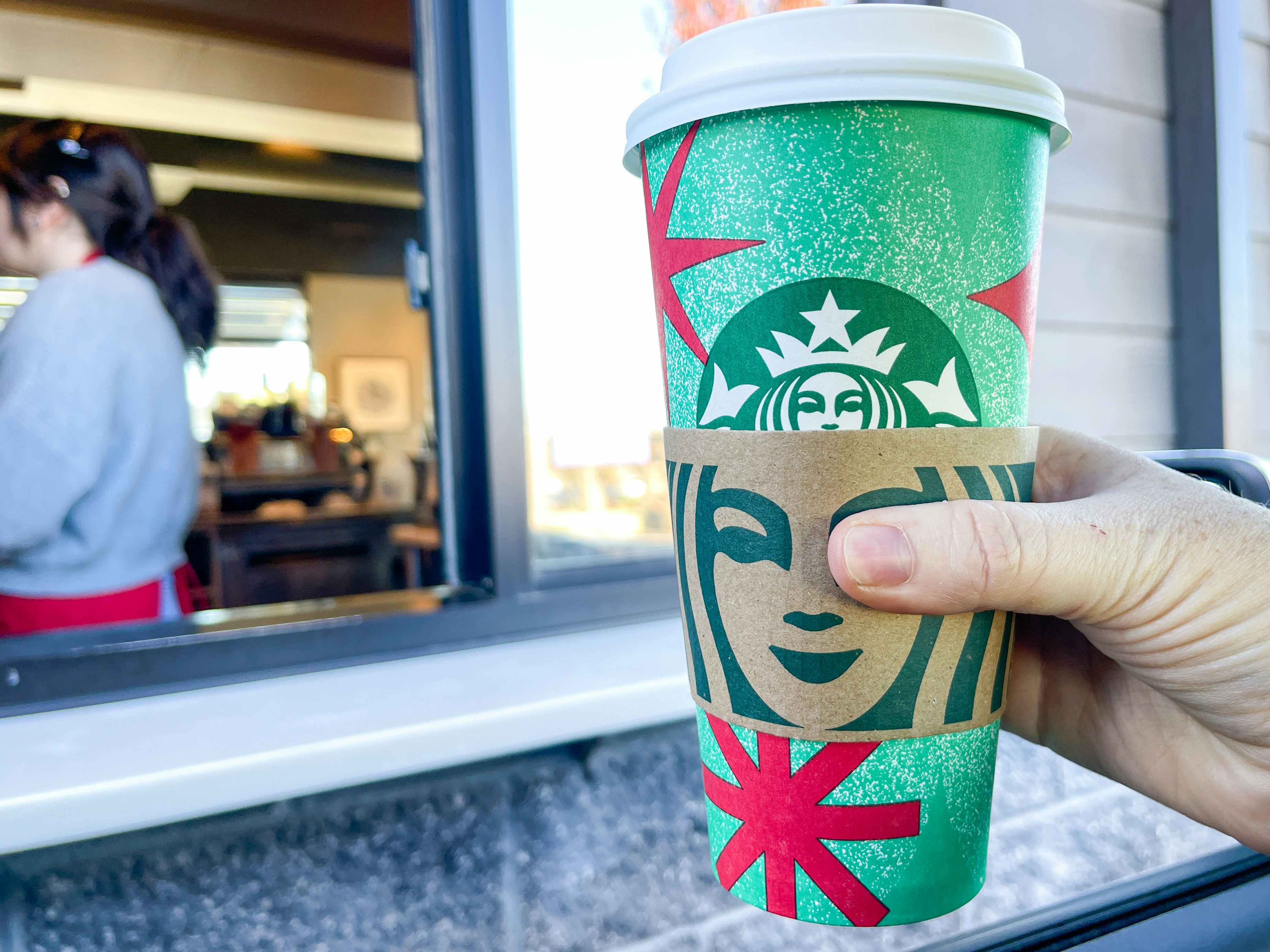 a person's hand holding up a starbucks holiday drink outside drive thru