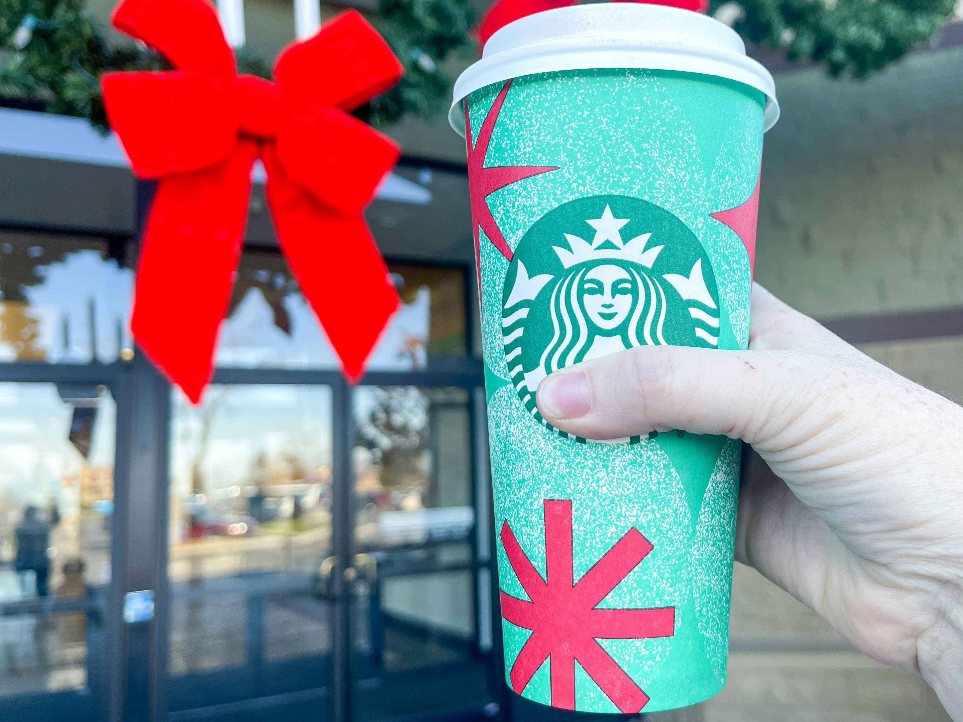 a person's hand holding up a starbucks holiday drink outside drive thru holiday wreath