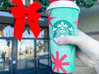 a person's hand holding up a starbucks holiday drink outside drive thru holiday wreath
