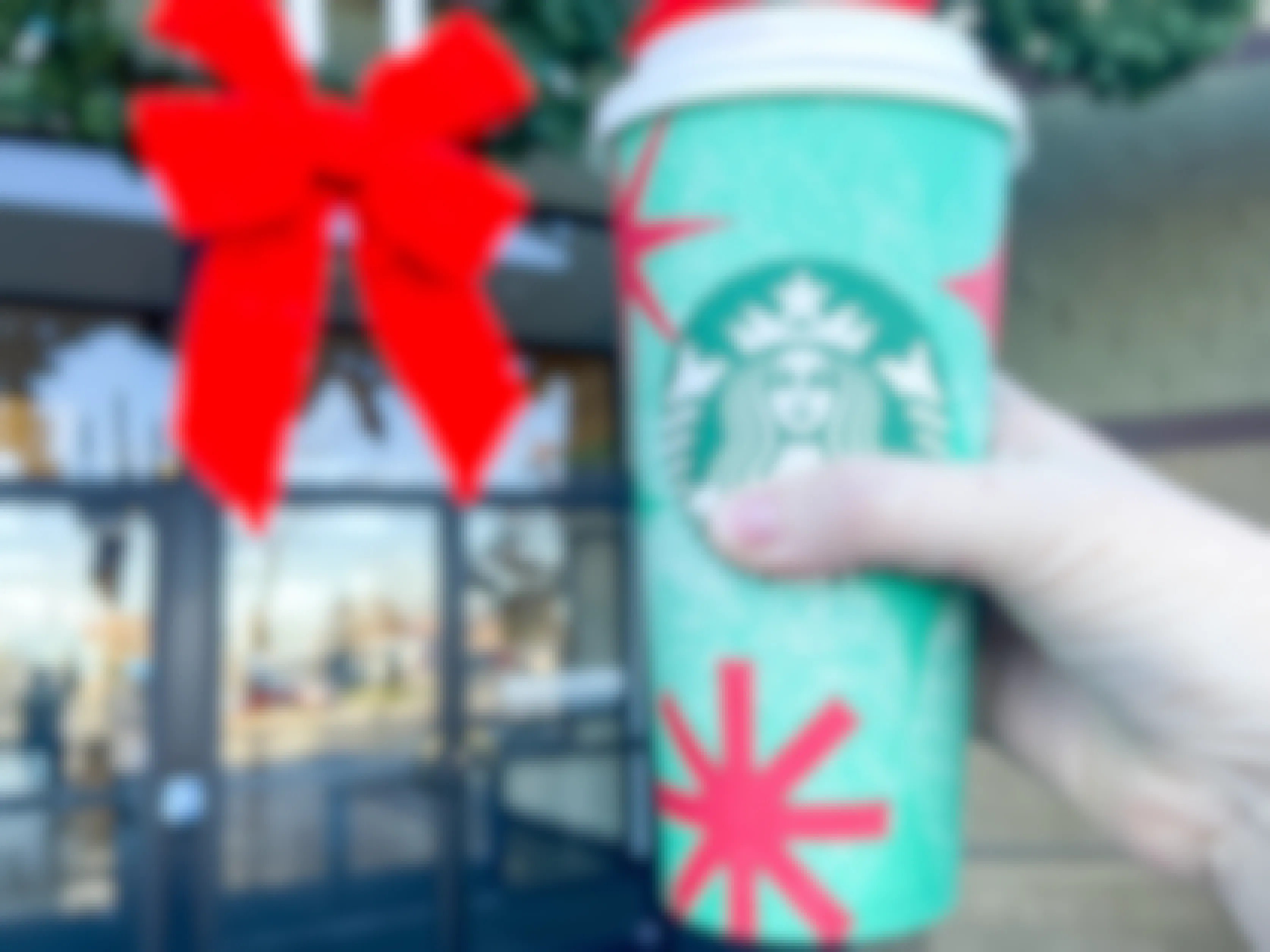 a person's hand holding up a starbucks holiday drink outside drive thru holiday wreath