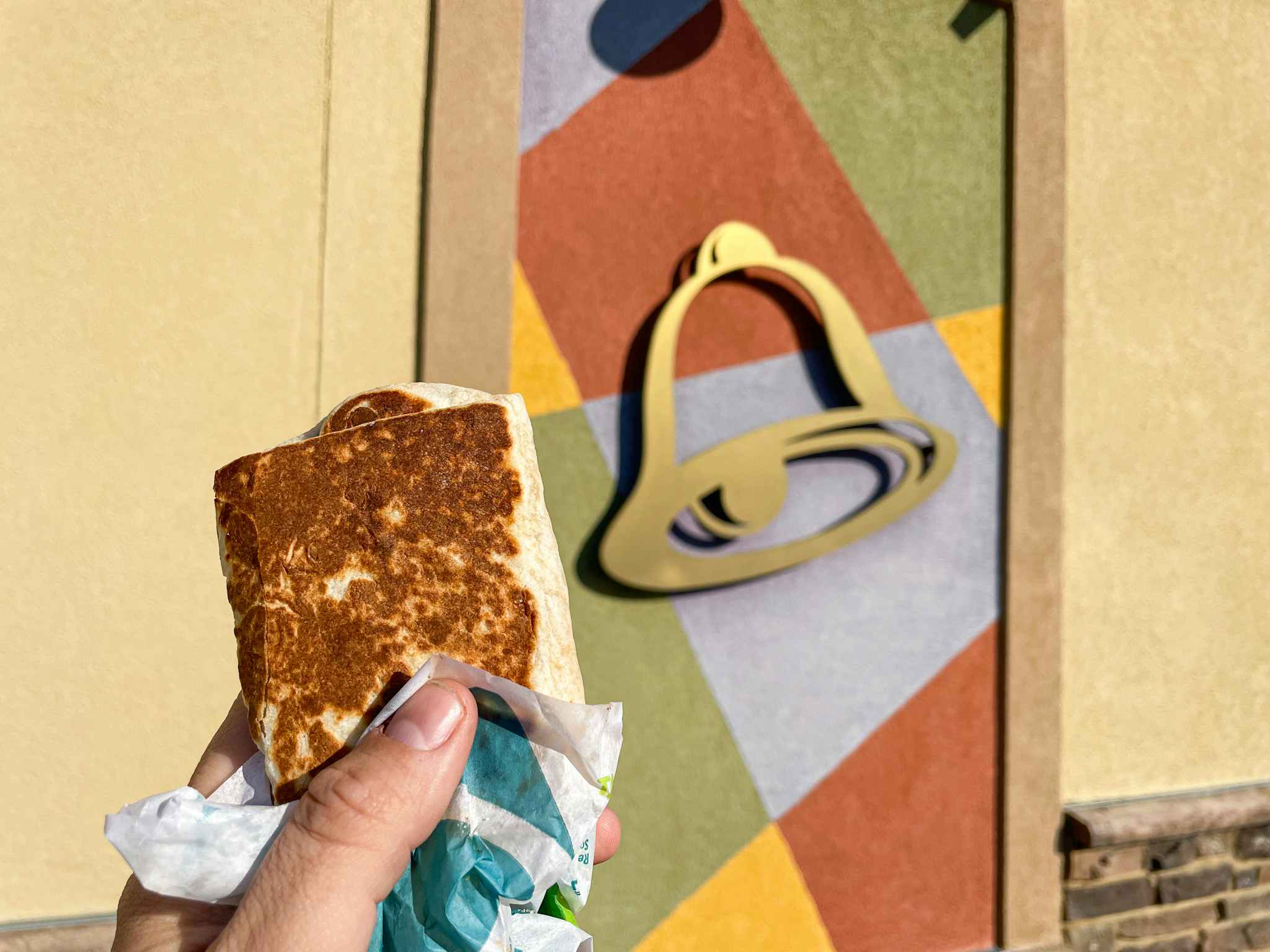 person holding taco bell burrito next to restaurant exterior