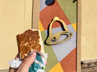 person holding taco bell burrito next to restaurant exterior