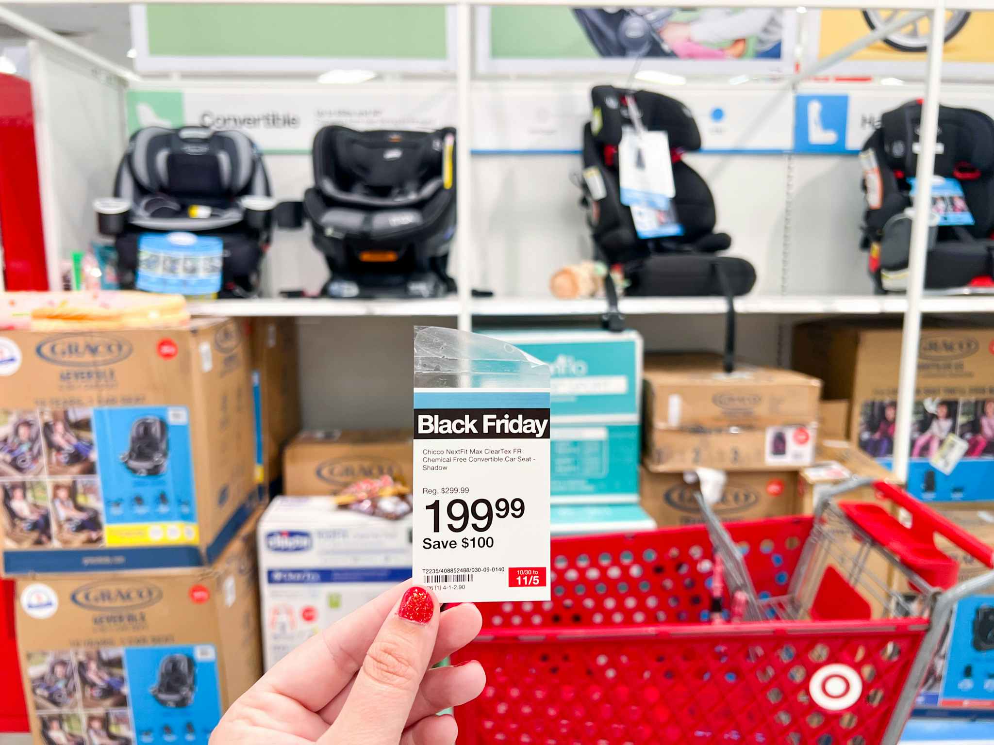 a woman's hand holding up a $199 Black Friday sale price tag at Target in front of a shelf with car seats displayed