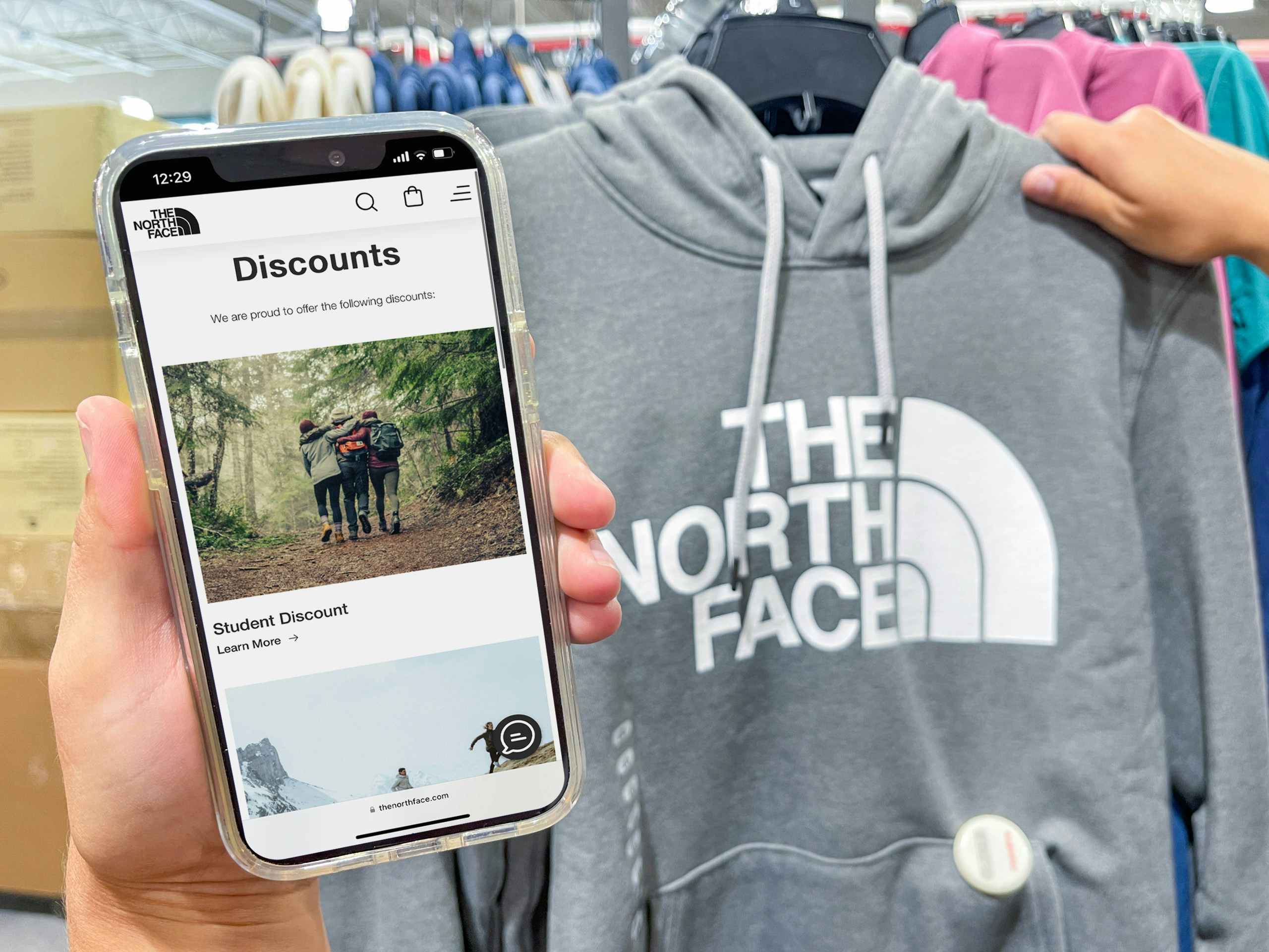 a person holding The North Face website on a cell phone next to a the North Face sweat shirt.