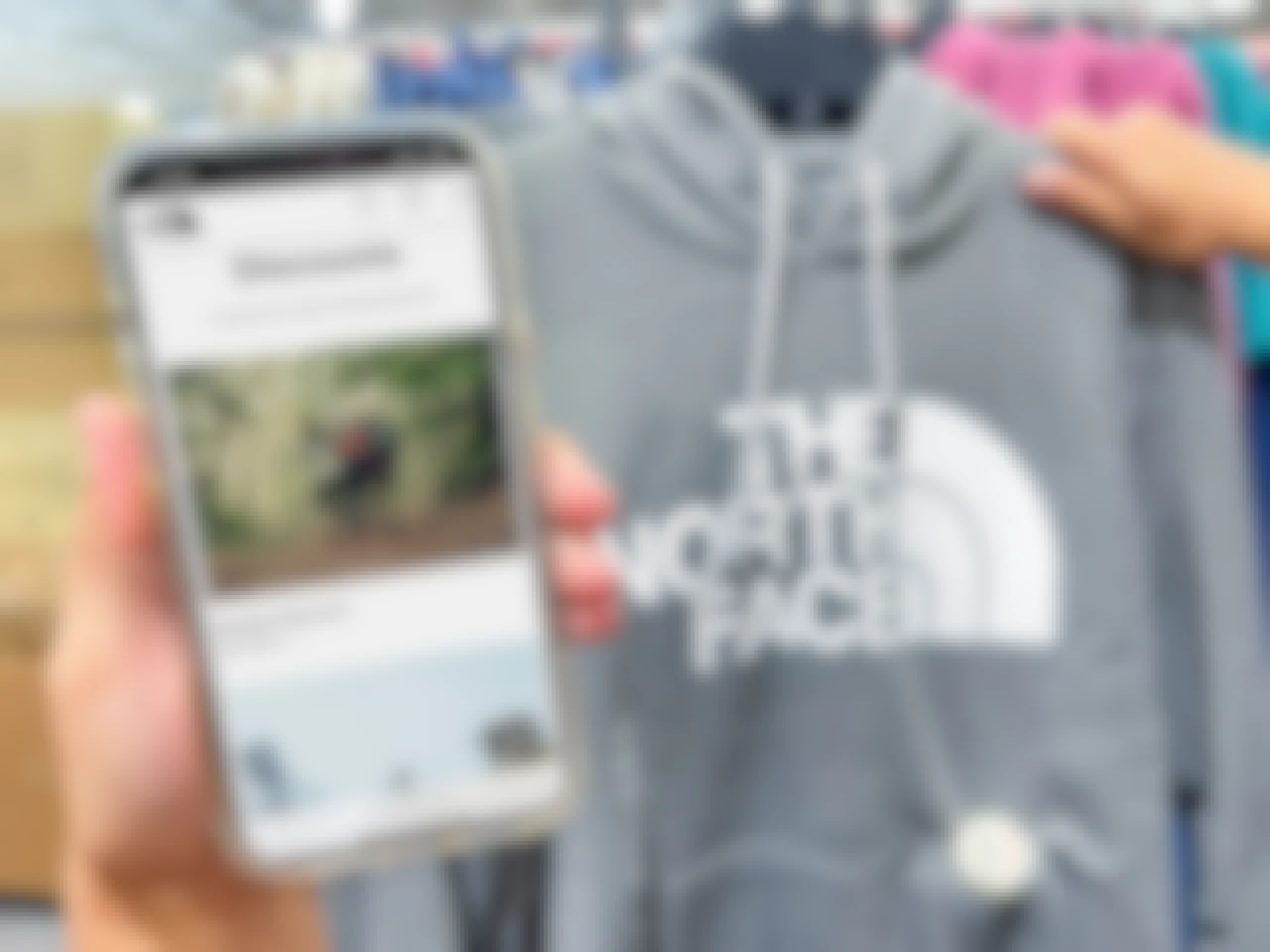 a person holding The North Face website on a cell phone next to a the North Face sweat shirt.