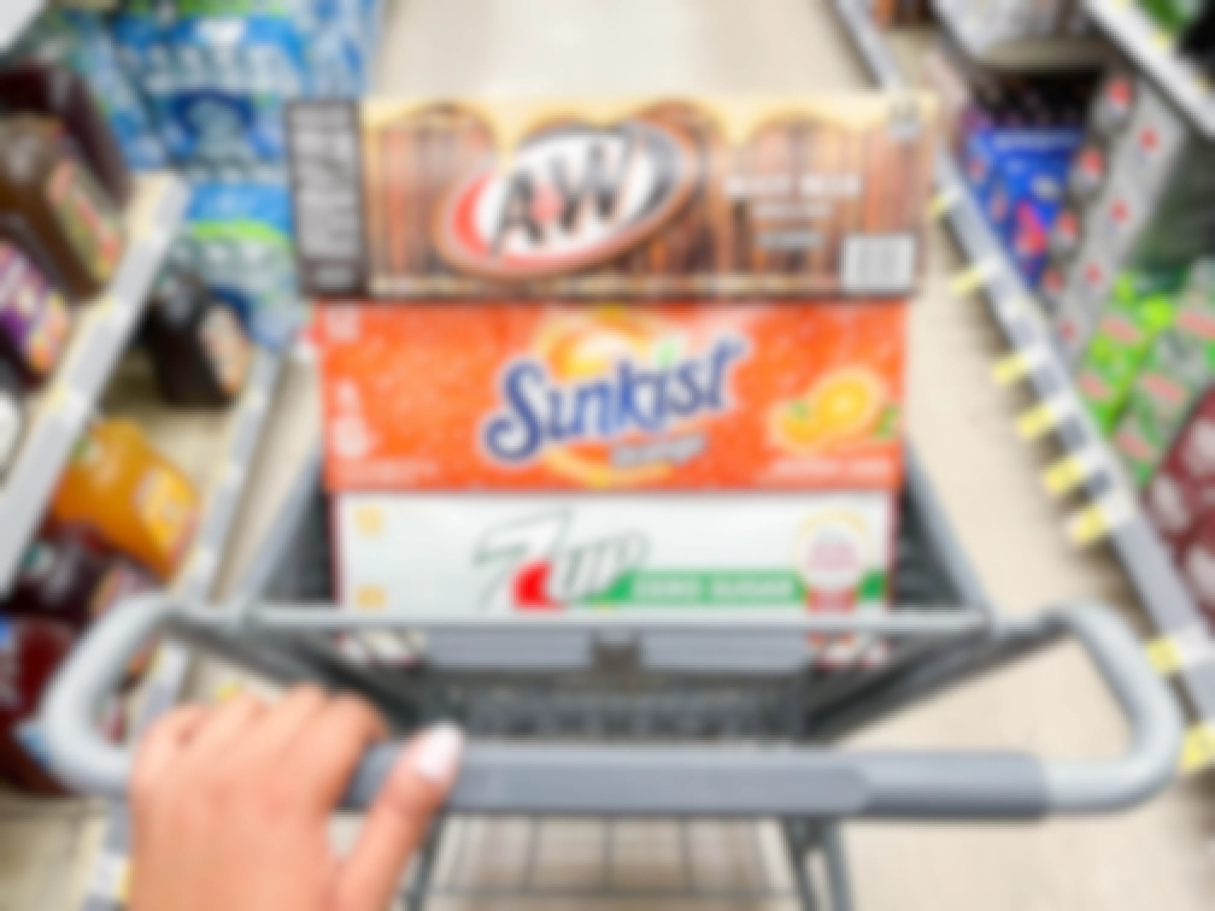 hand pushing shopping cart with A&W, Sunkist, and 7-Up 12-packs inside