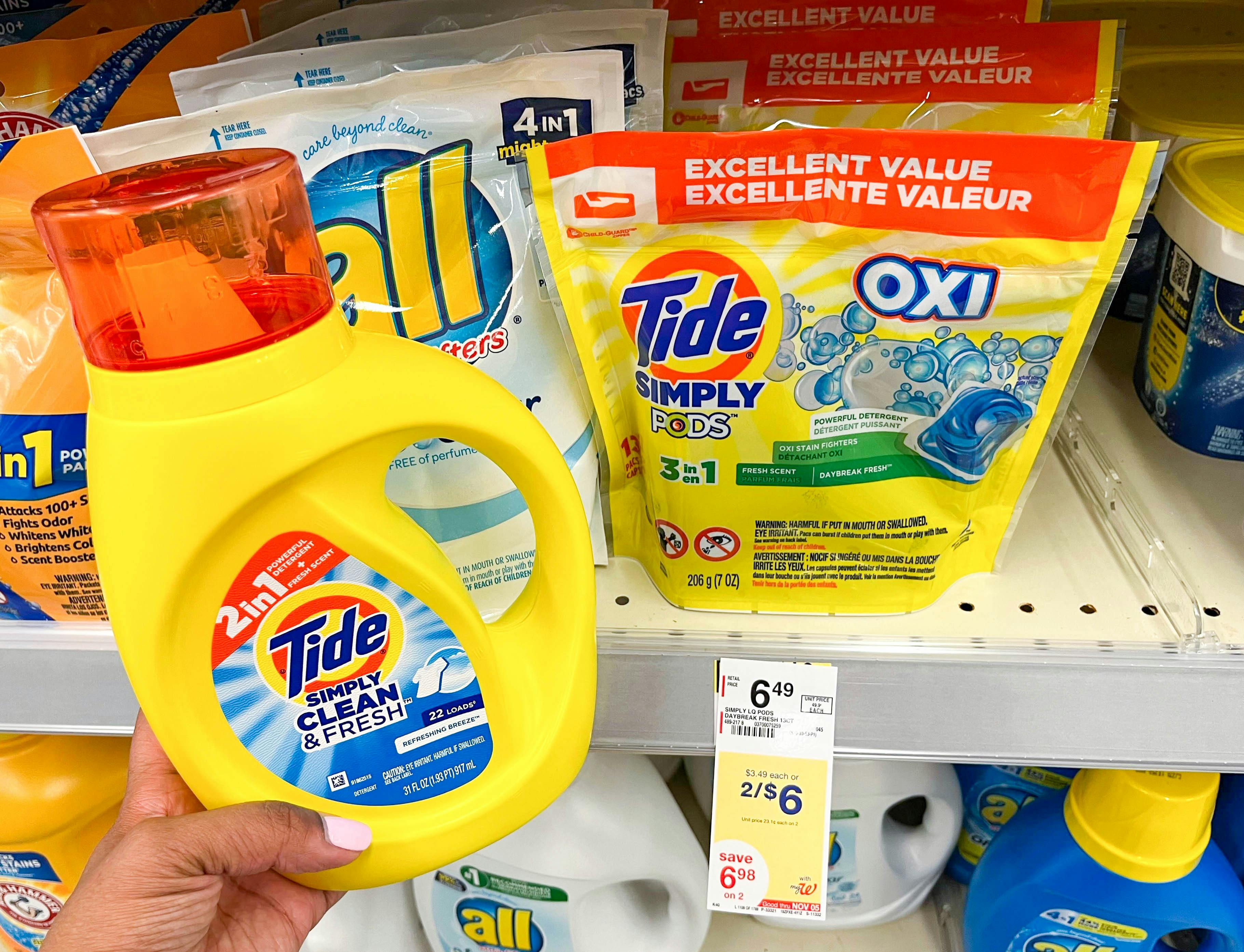 hand holding one bottle of Tide Simply liquid laundry detergent next to Tide Pods on shelf with sales tag underneath