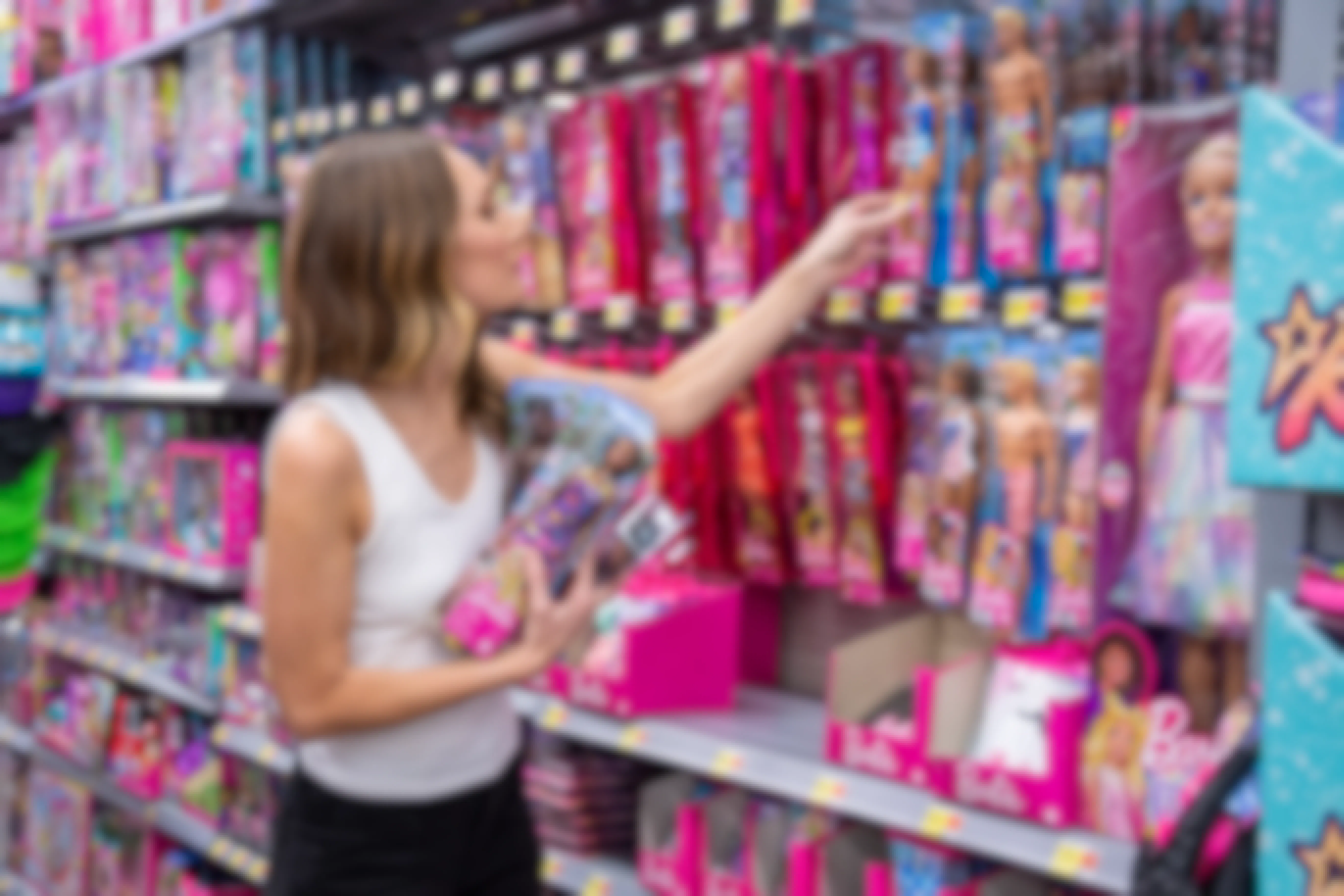 A woman reaching for barbie dolls hanging on the shelf at Walmart