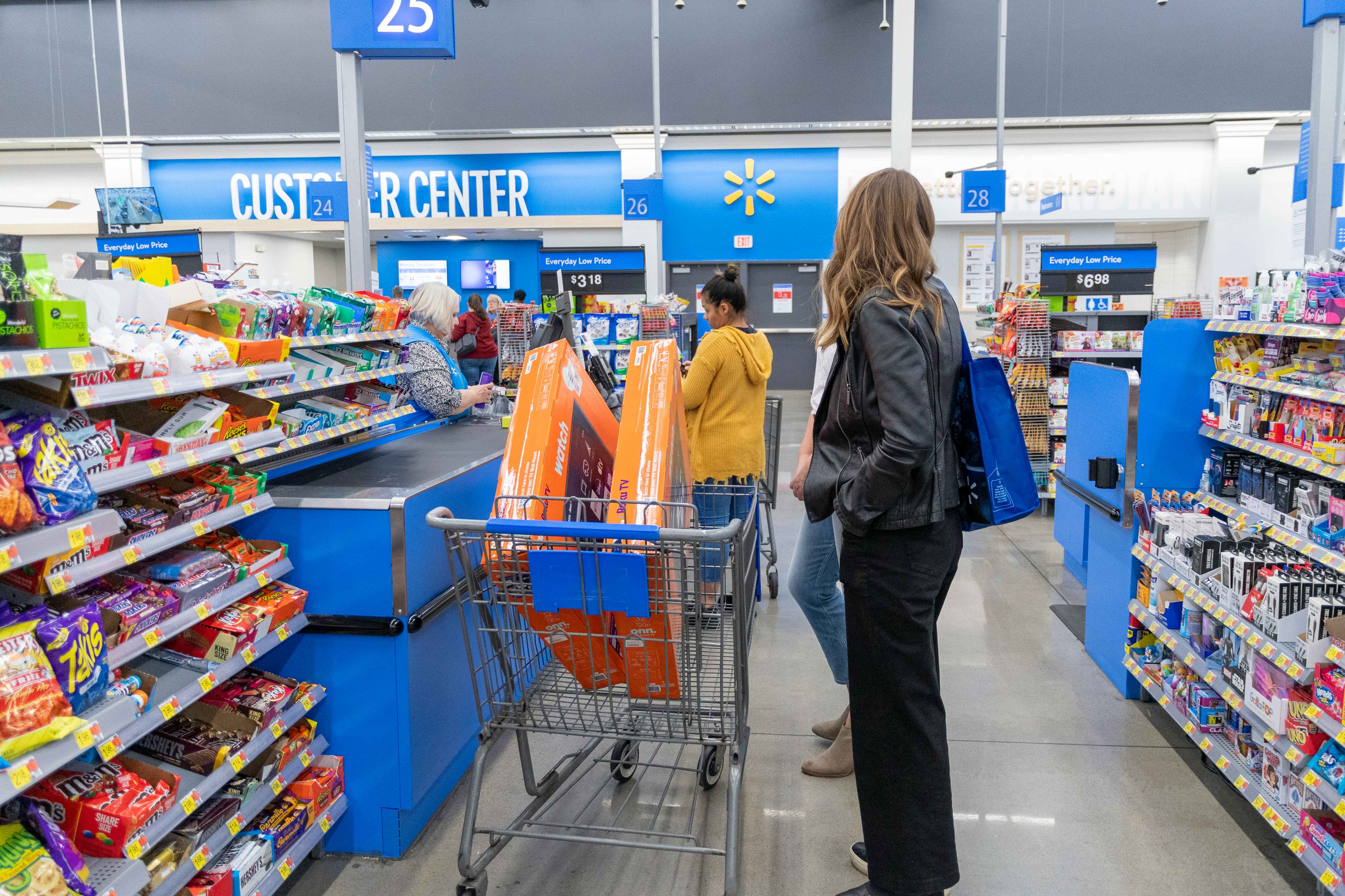 A woman standing with her Walmart cart at a Walmart checkout lane with two Roku TVs in her cart