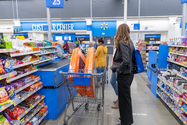 A woman standing with her Walmart cart at a Walmart checkout lane with two Roku TVs in her cart