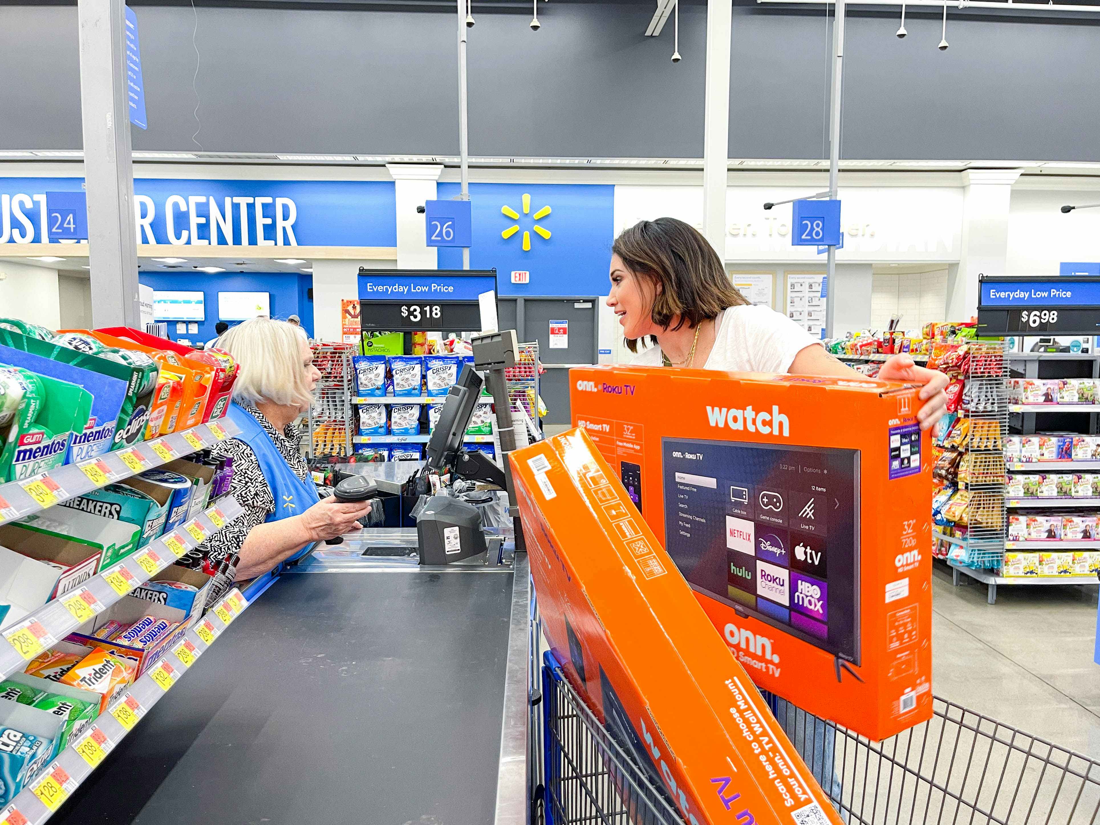 A woman talking to the cashier at Walmart checkout as she puts a TV on the conveyer