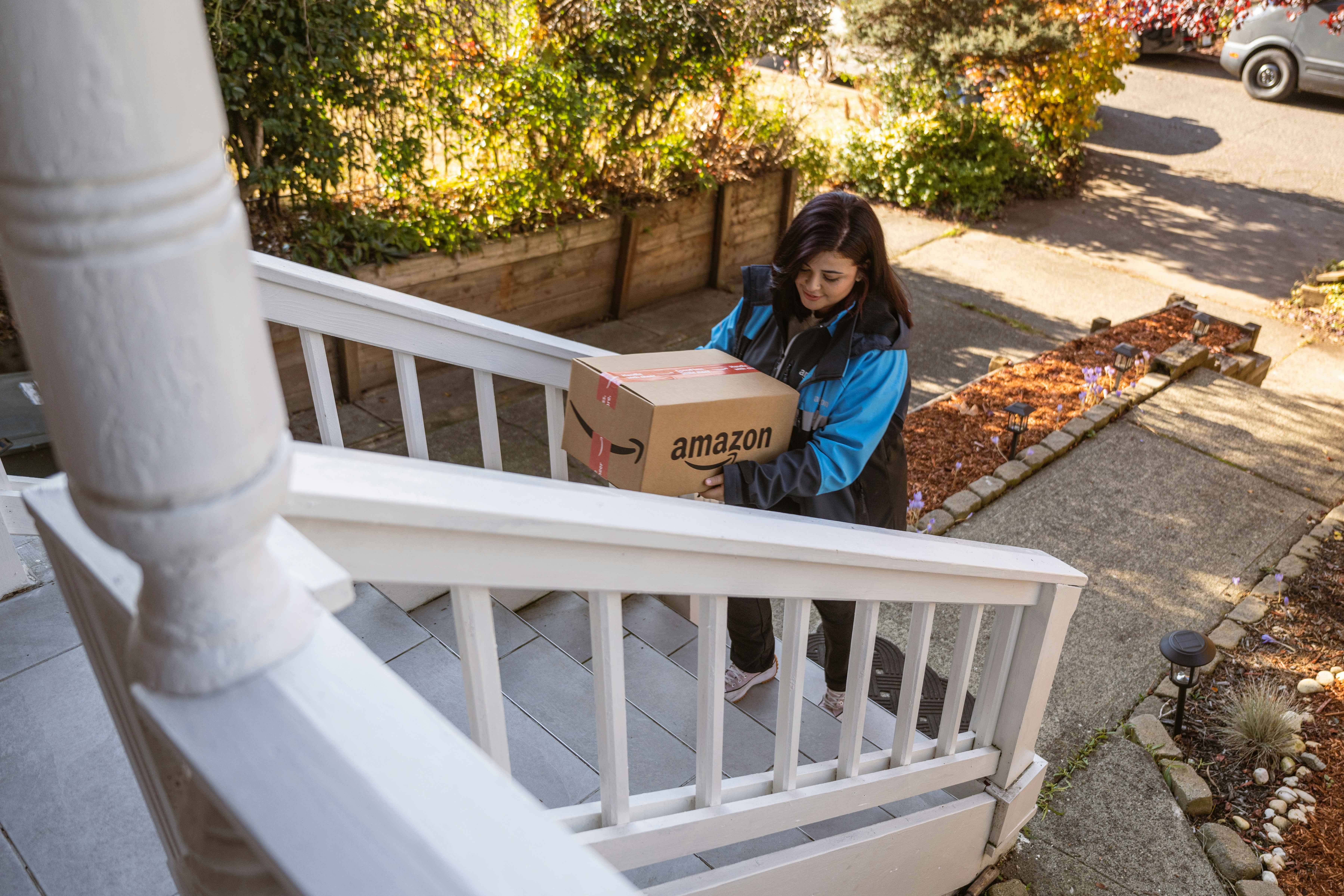 A delivery driver carrying an amazon box onto a front porch.