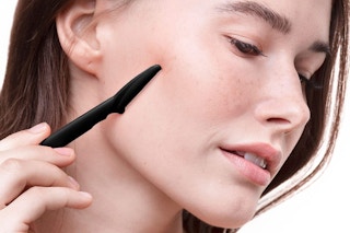 A woman dermaplaning her face.