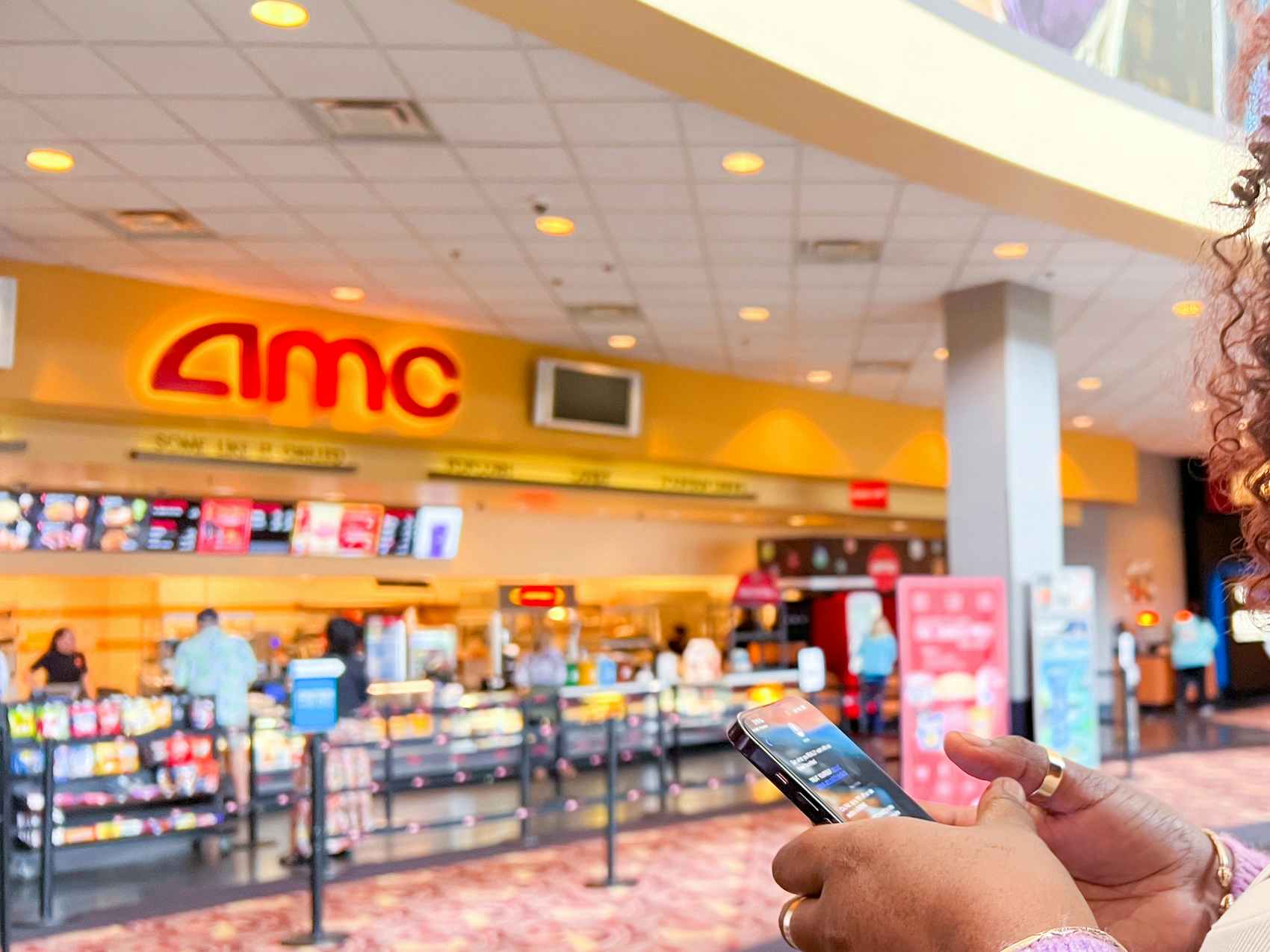 Someone looking at their phone while standing in an AMC theatre lobby