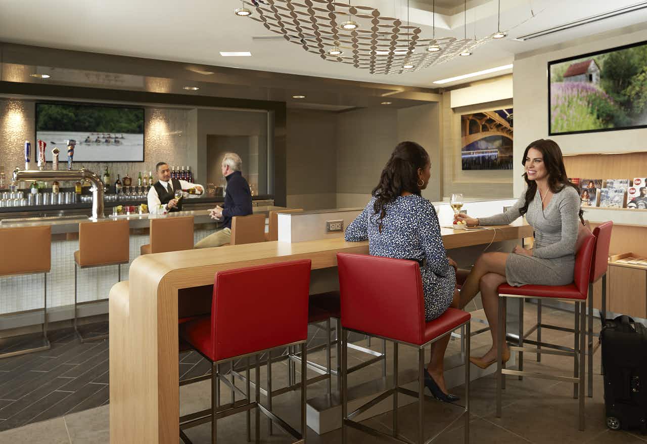 People sitting at the bar and hightop tables in the American Airlines Admiral's Club lounge area.