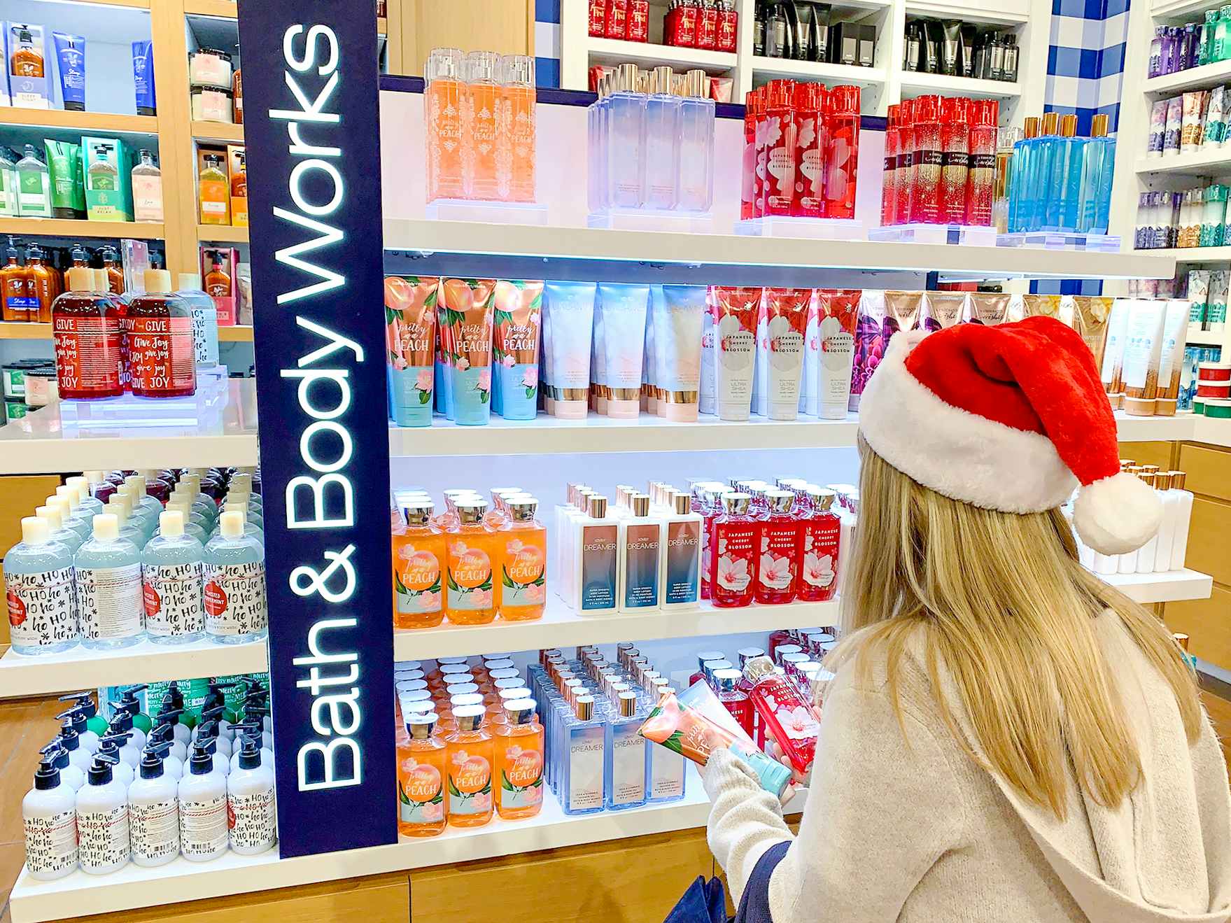 A woman in a santa hat looking at Body care items at bath and body works