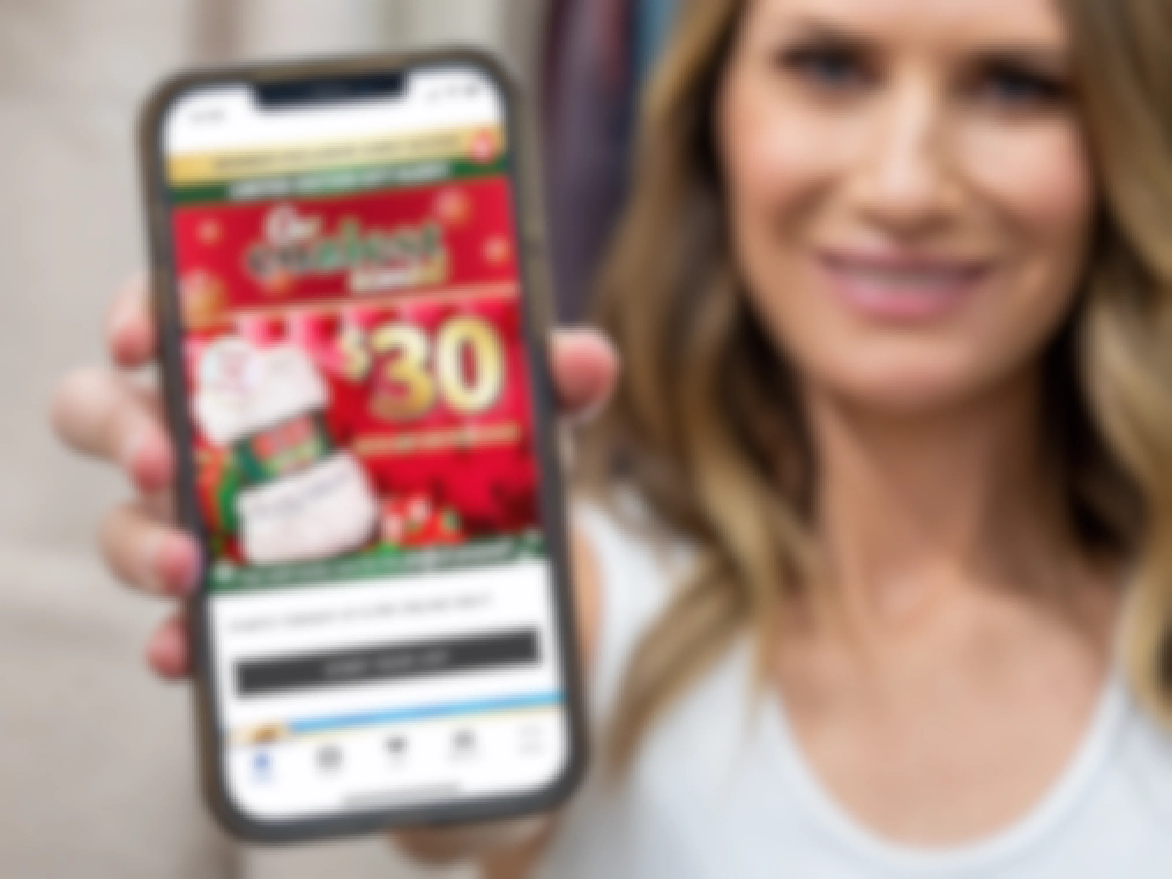 A person holding out a cell phone displaying the Bath & Body Works rewards app ad for the $30 blanket with a $45 purchase.