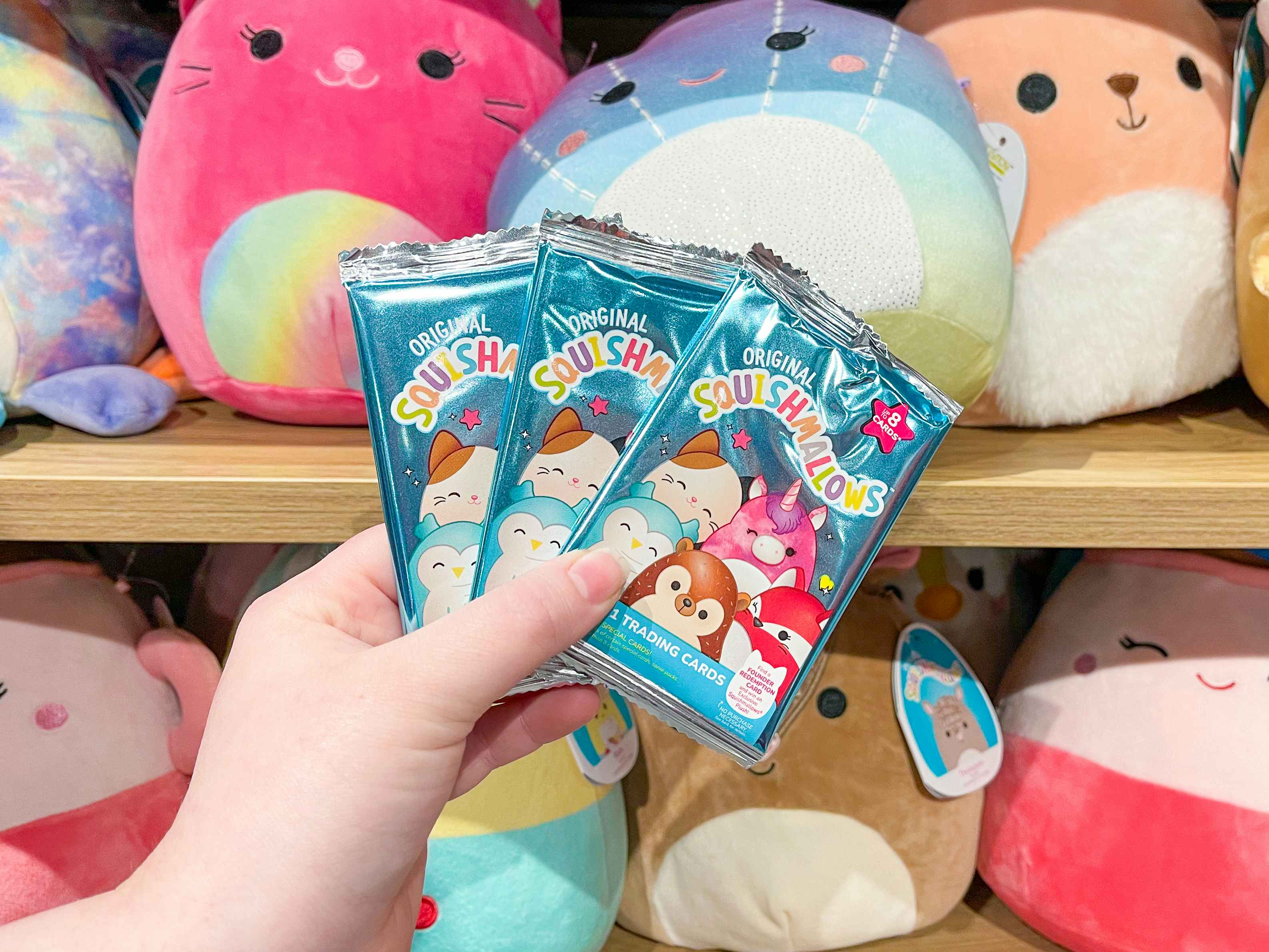 A person's hand holding up some Squishmallows trading card packs