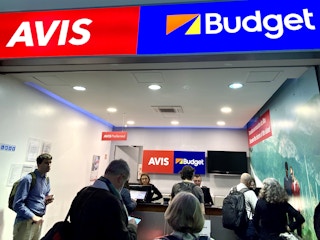 avis and budget sign above a line of people waiting at the counter