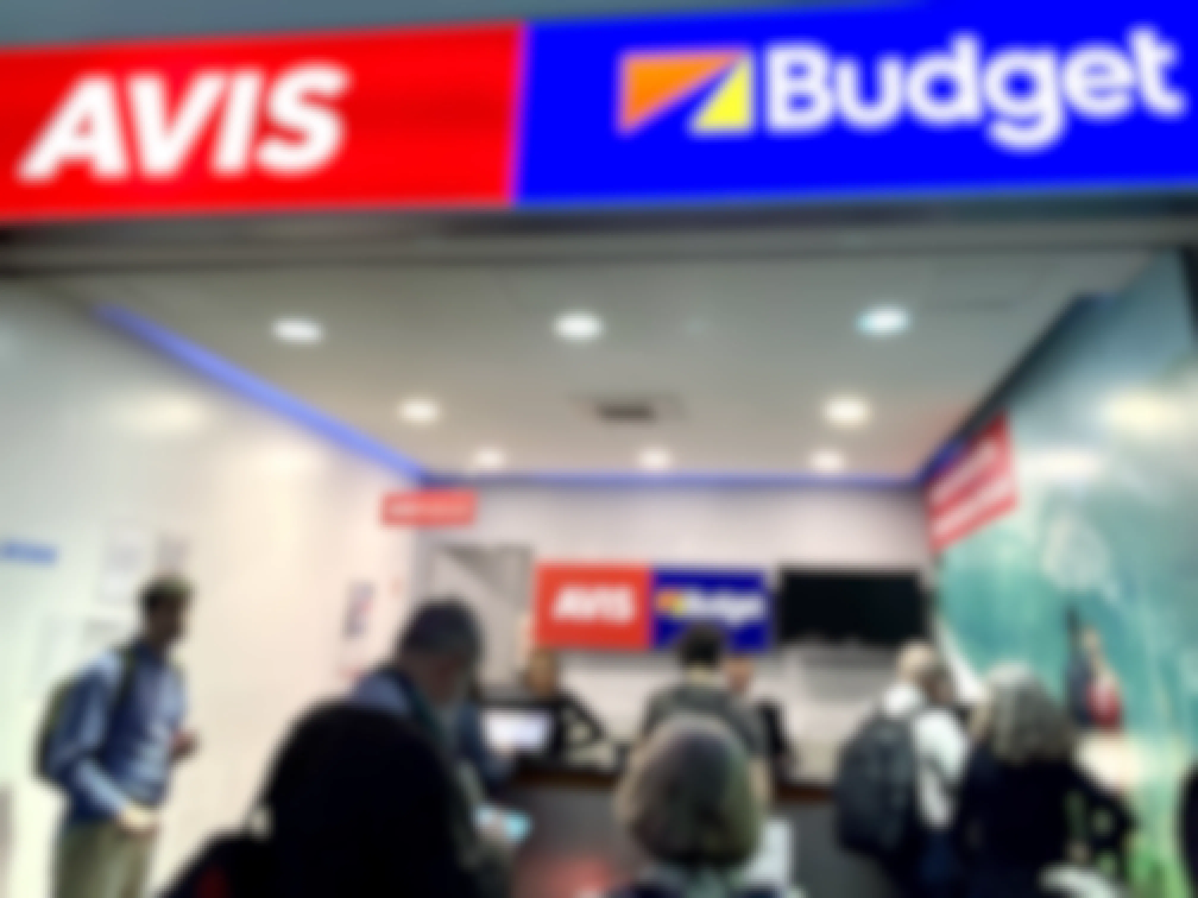 avis and budget sign above a line of people waiting at the counter
