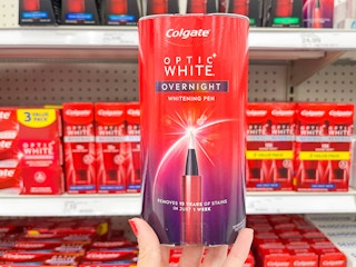 A Colgate Optic White Overnight Whitening pen held out by hand in front of other Colgate products sitting on a store shelf.