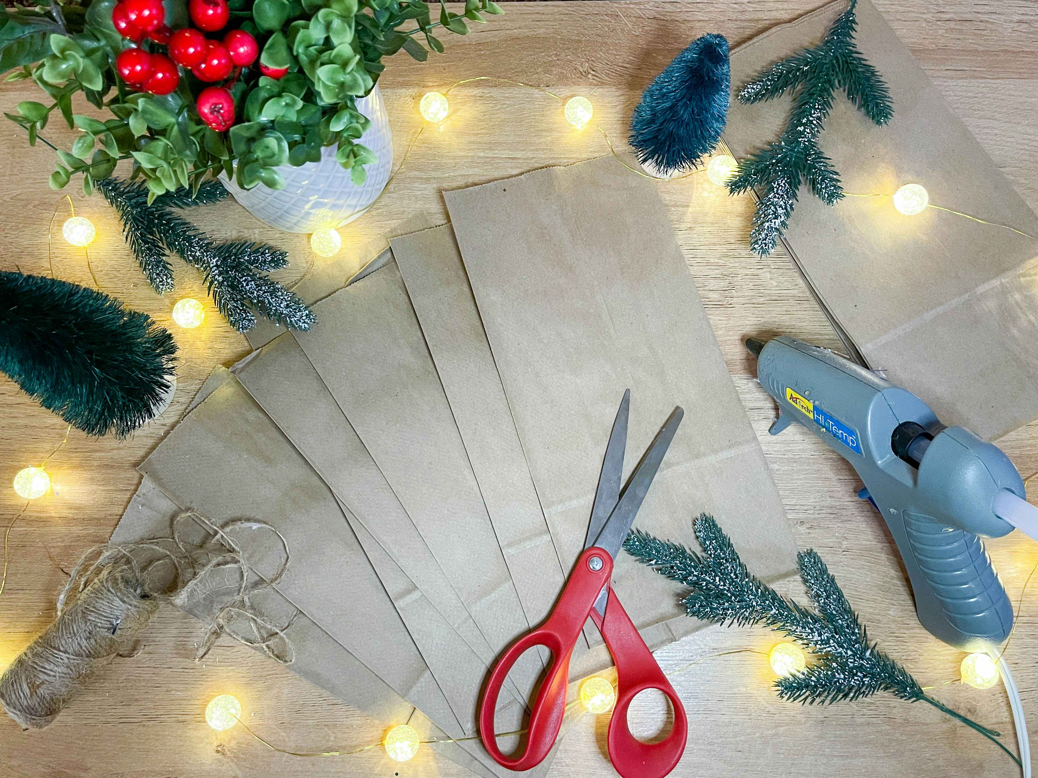 brown paper bags sitting on a counter with christmas decor, glue gun. and scissors on the table 