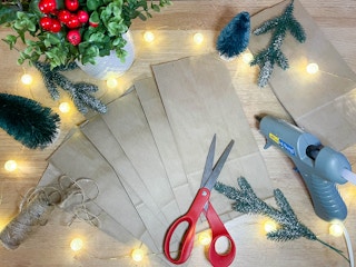 brown paper bags sitting on a counter with christmas decor, glue gun. and scissors on the table 