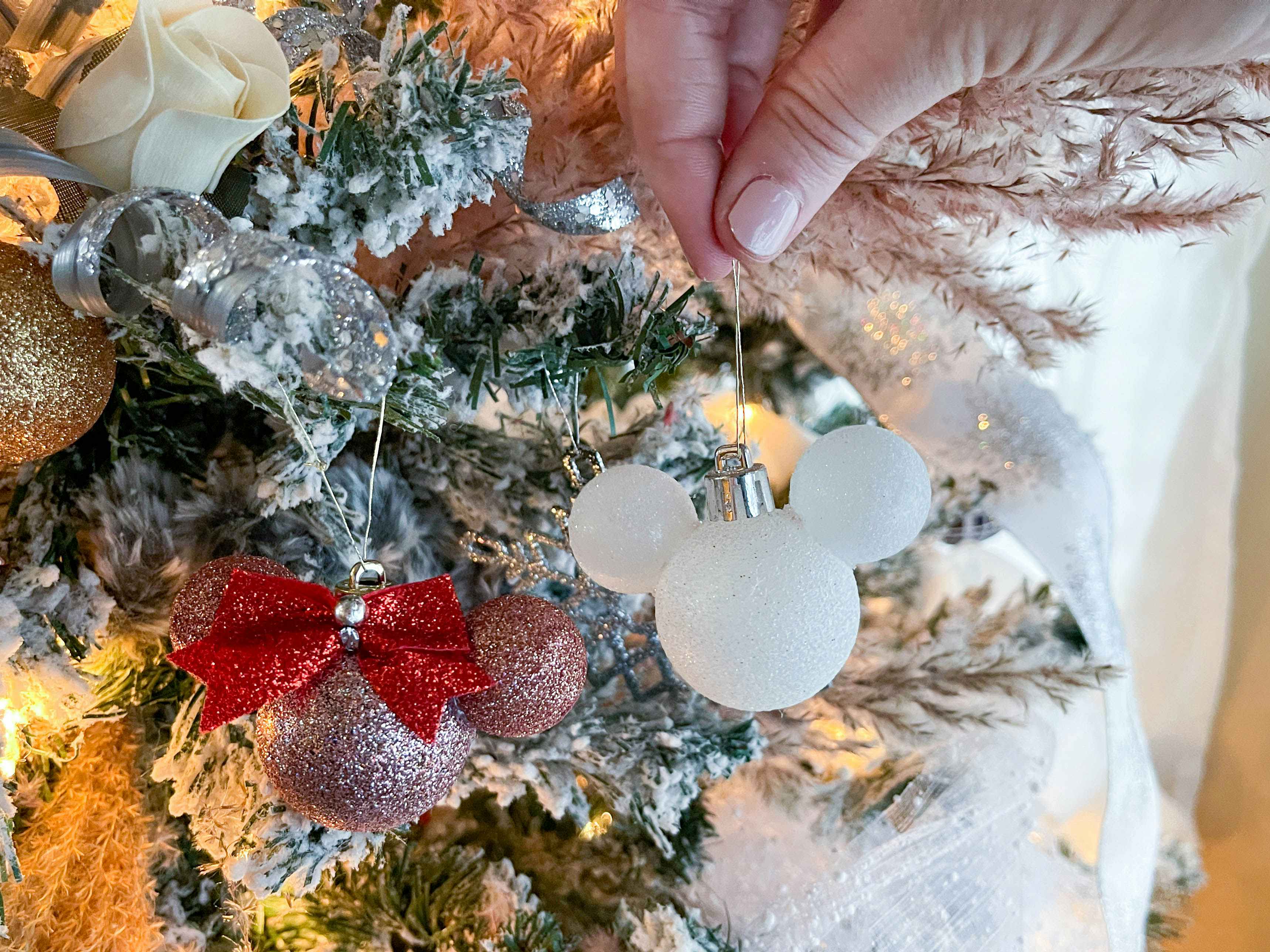 a persons hand handing mouse ornaments on a christmas tree 