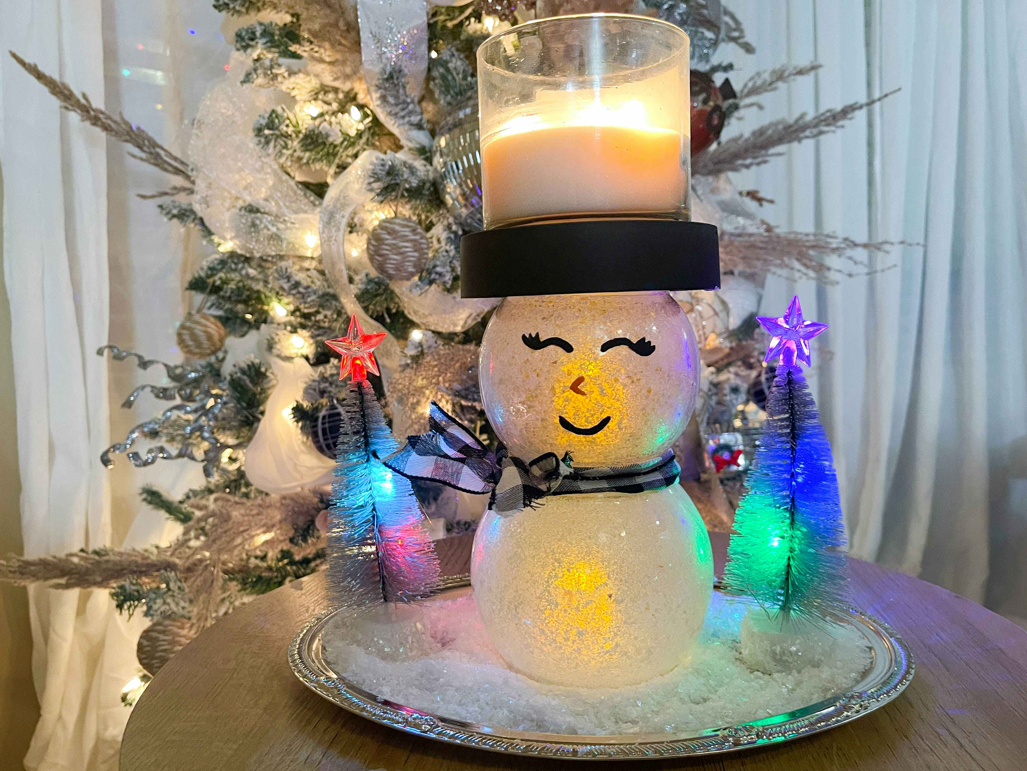 a diy snowman candle holder on a table in front of a chrsitmas tree