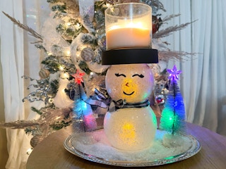 a diy snowman candle holder on a table in front of a chrsitmas tree