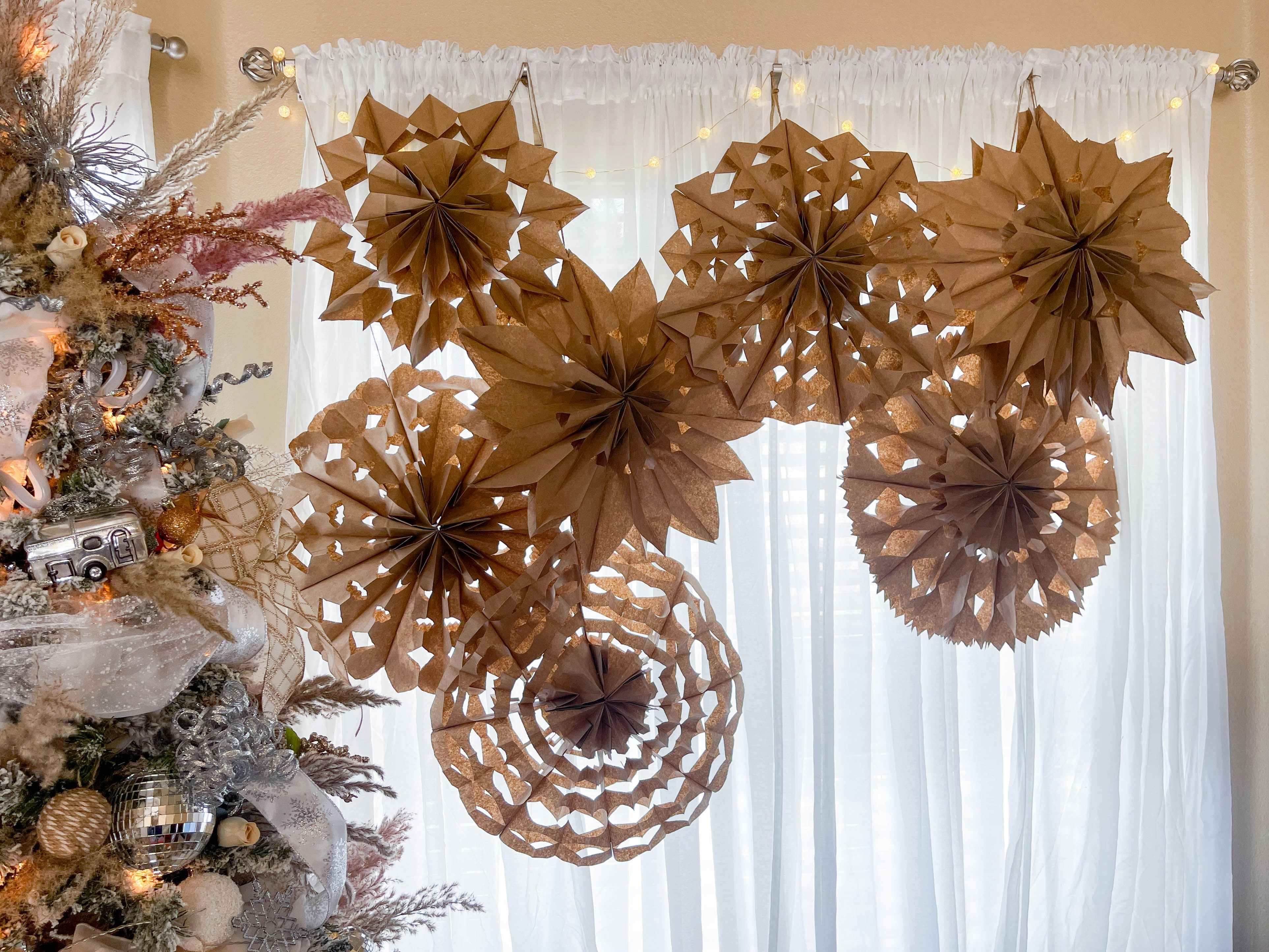a bunch of paper bag snowflakes hanging in a window 