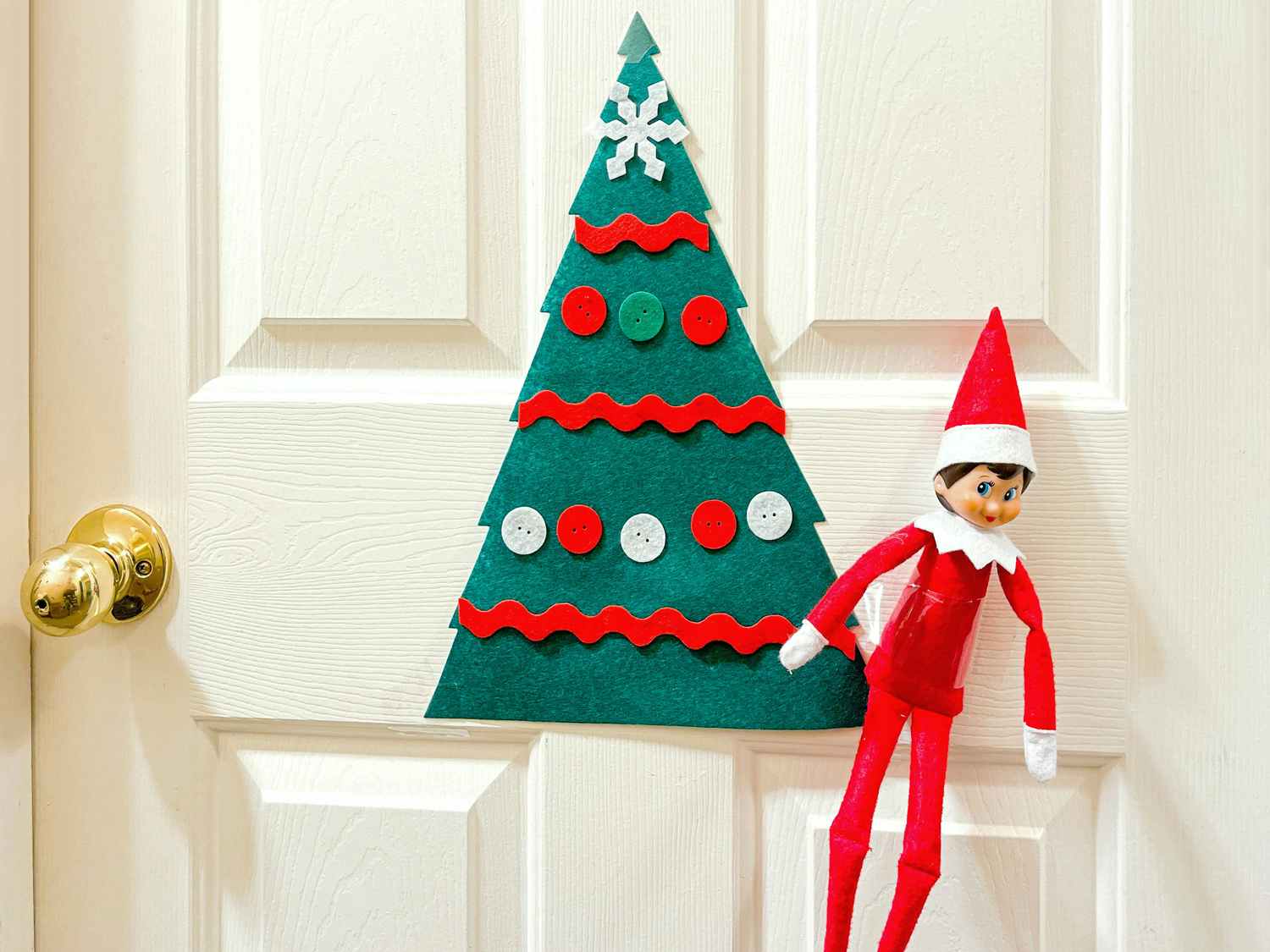 elf on the shelf hanging with decorated felt tree on door
