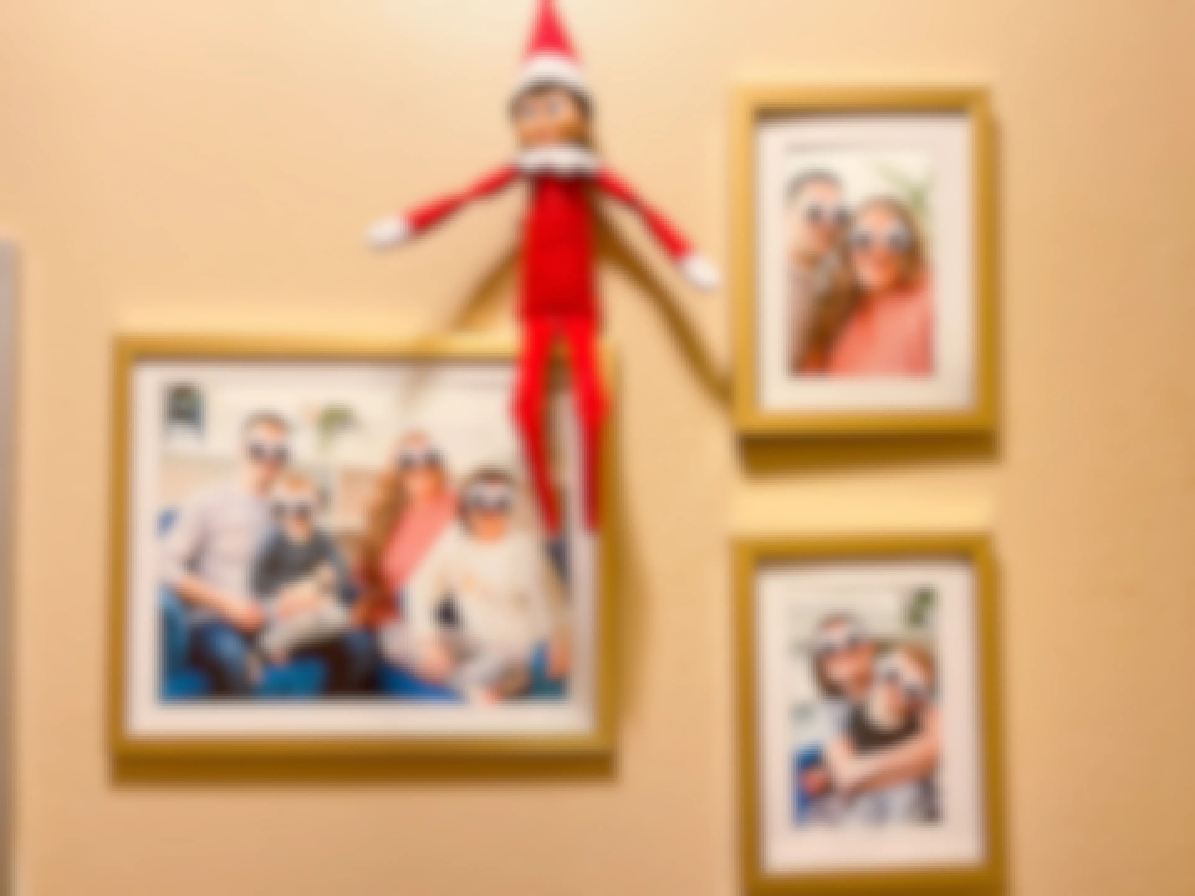 elf on the shelf doll sitting on picture frames on the wall with googly eyes over the faces on a family 