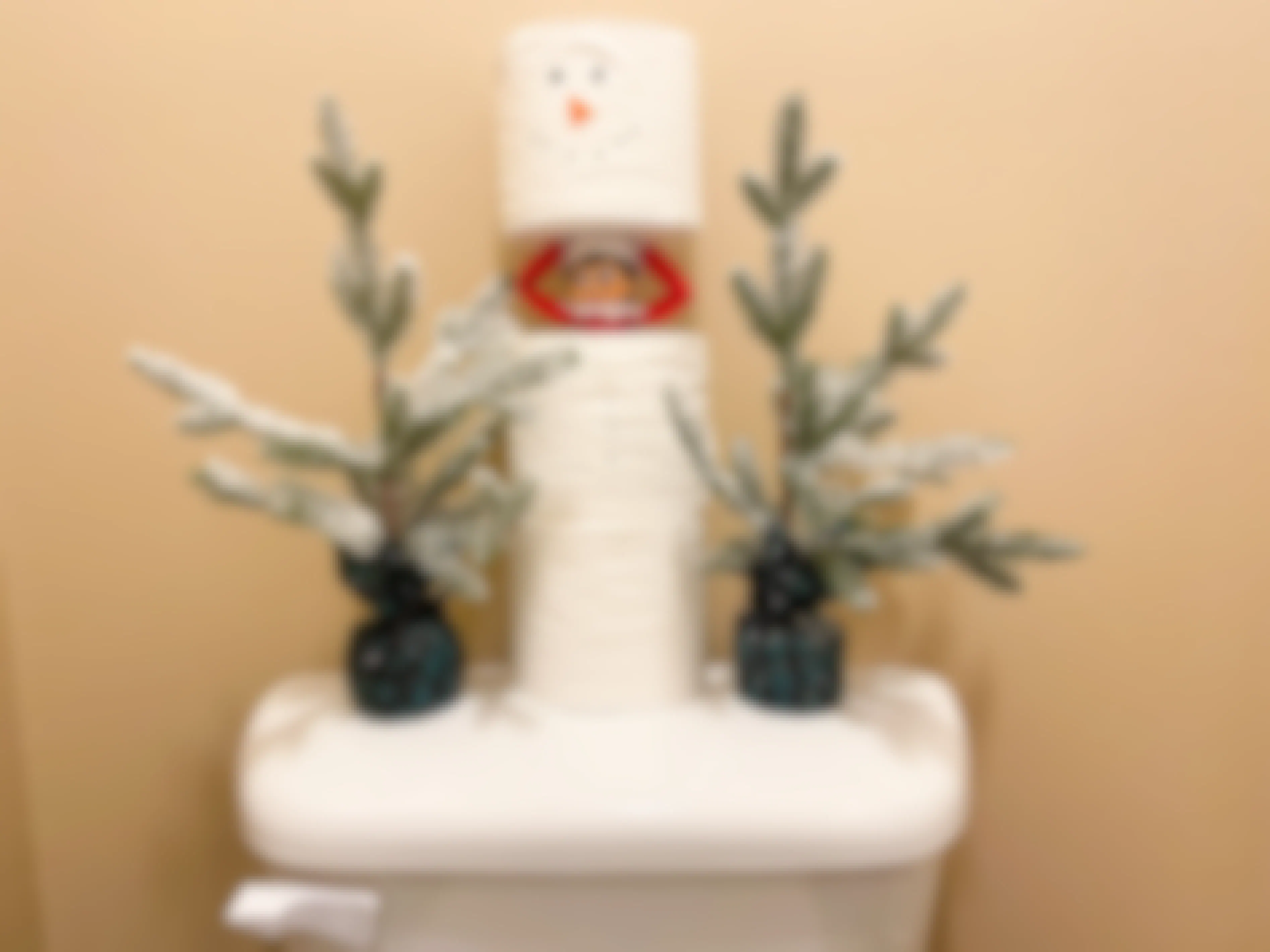 elf on the shelf hiding in stacked toilet paper made into a snowman 