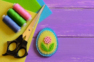 Felt easter egg floral craft with thread and a pair of scissors beside it.