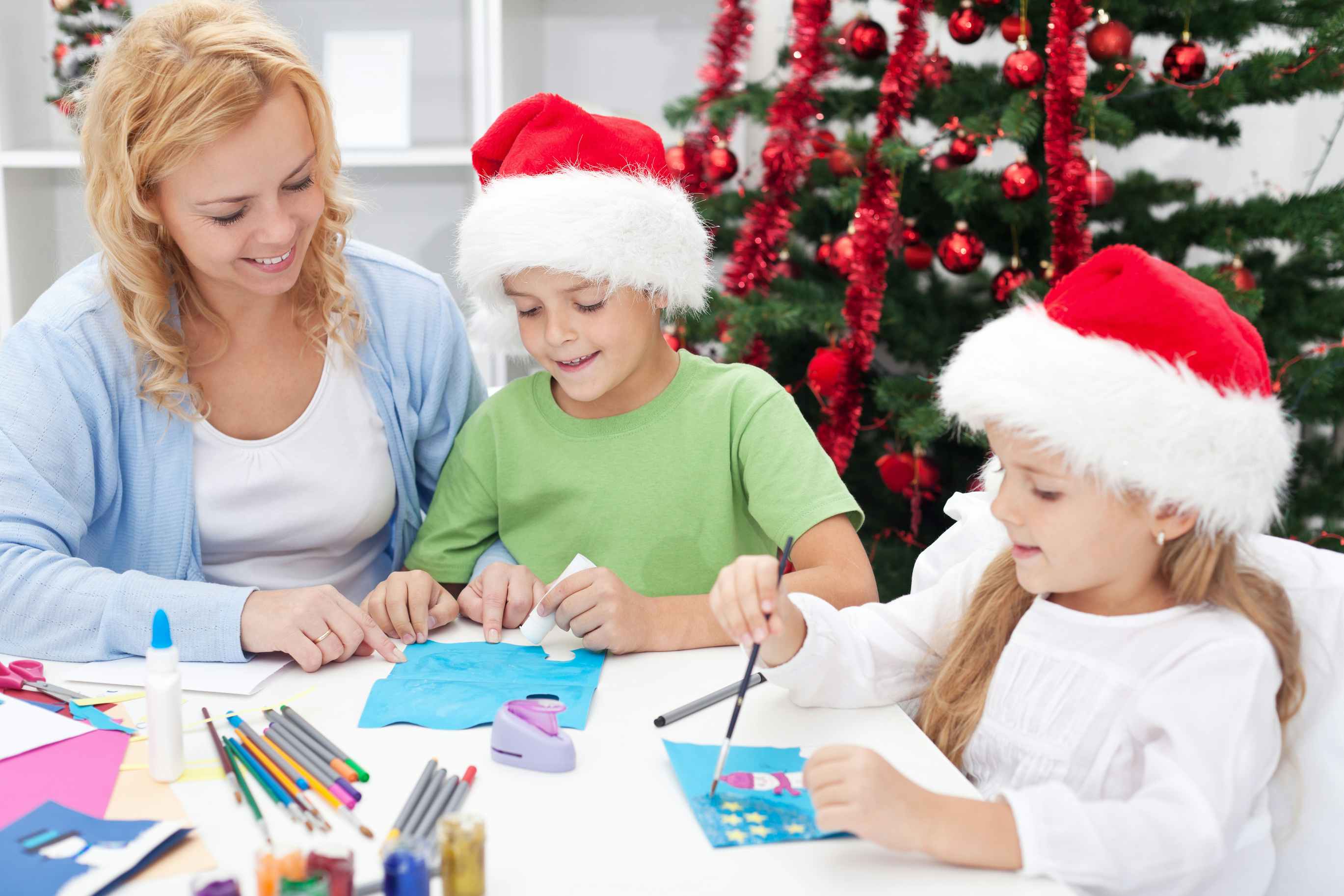 A mom and her kids sitting at a table, the children both working on some art for a holiday gift