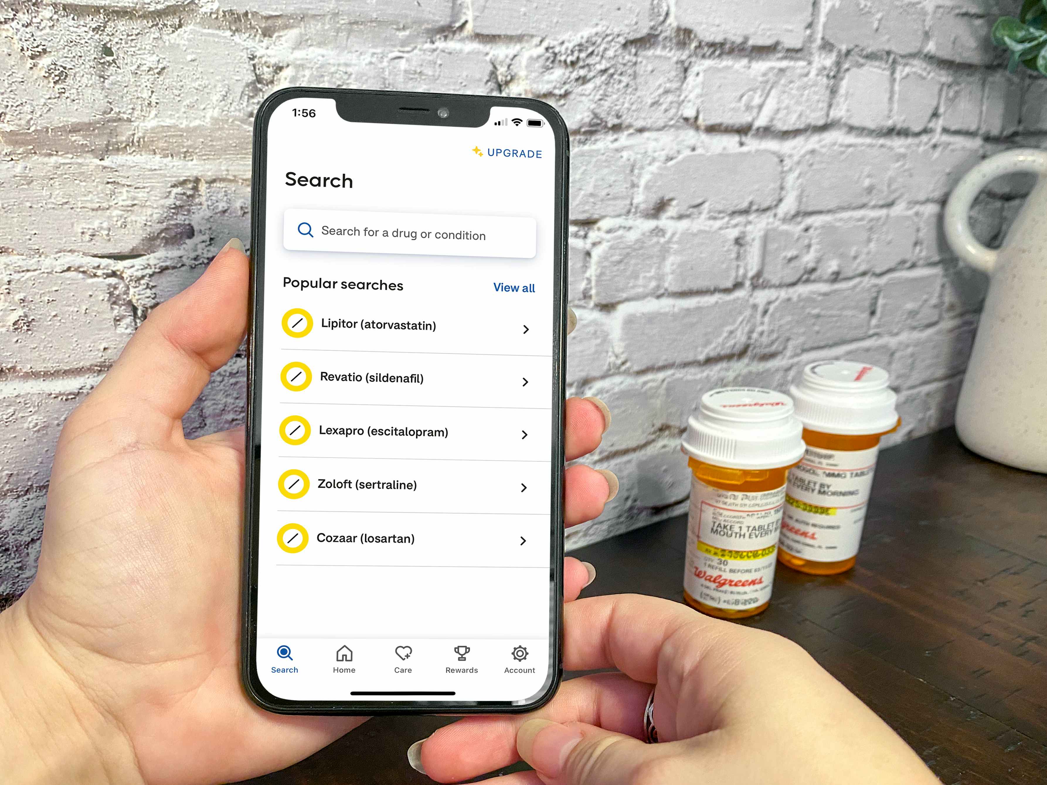 Someone holding a cell phone displaying the GoodRx app search screen next to some prescription medications on a table