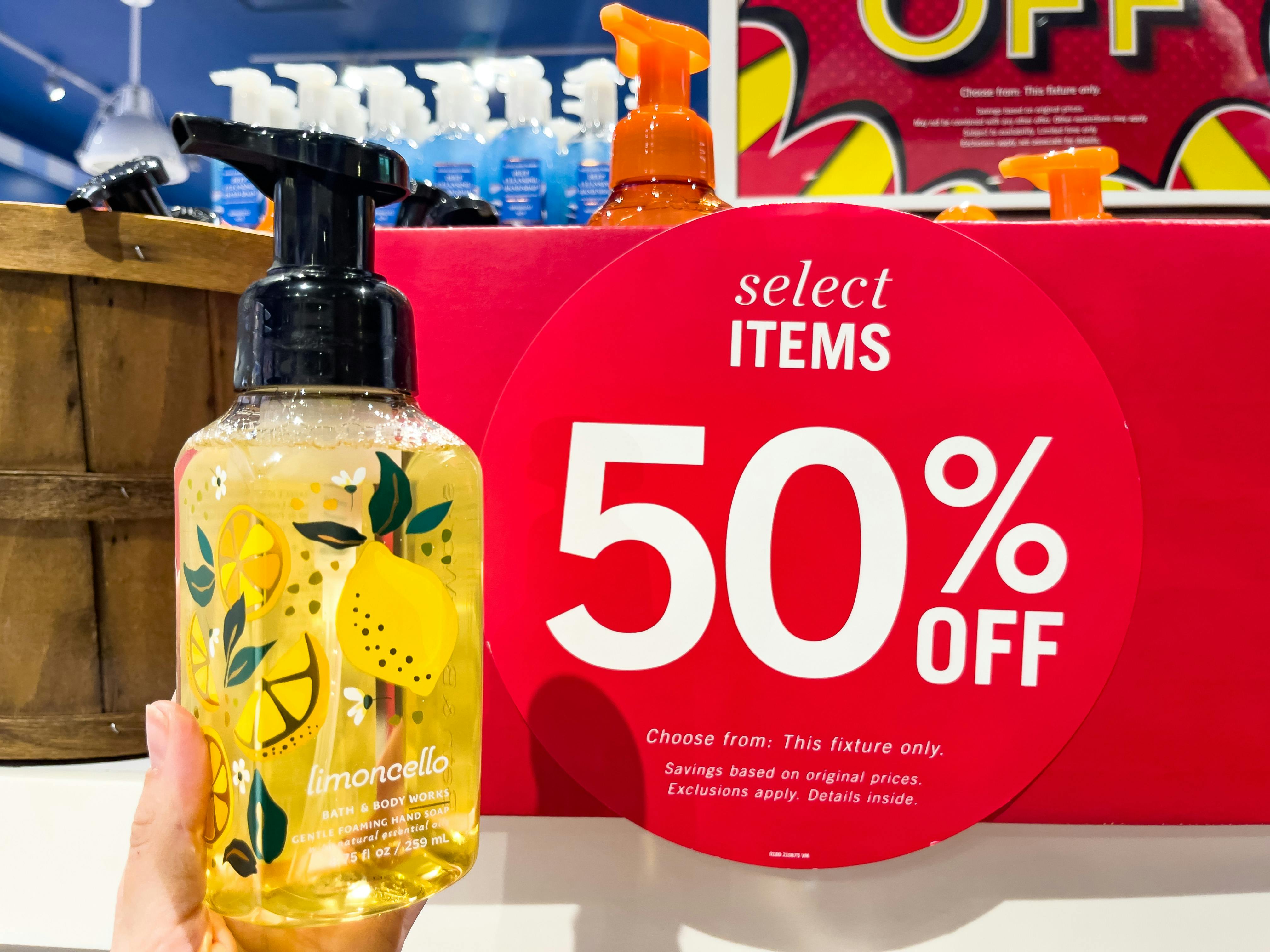 A hand soap held out by hand in front of a 50% off sign.