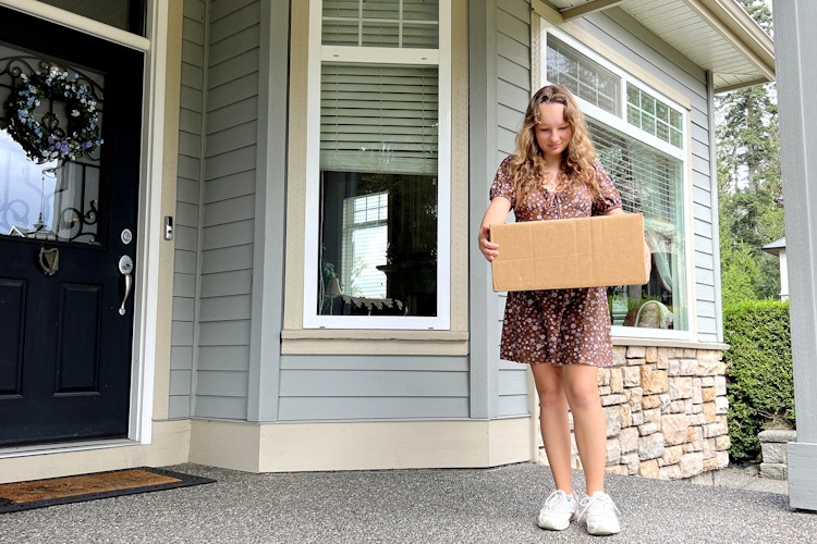 A person standing on a front porch with a shipping box