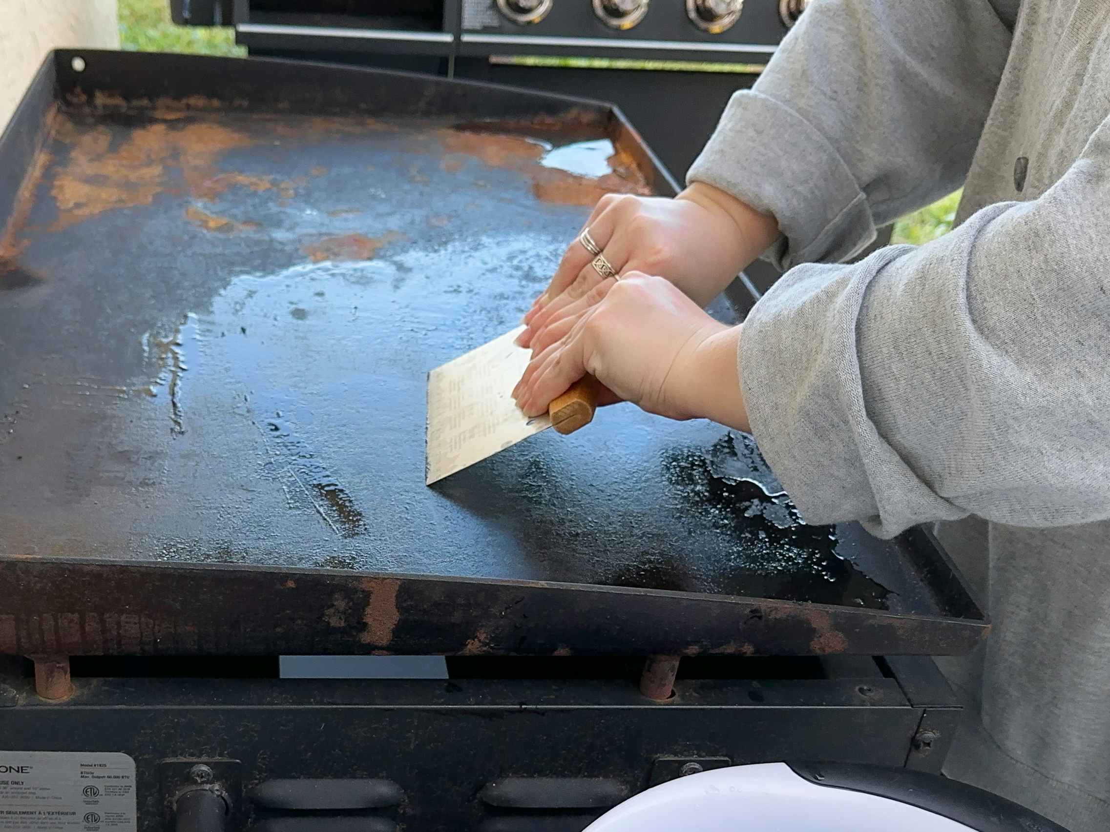 Someone scraping food debris off of a Blackstone griddle