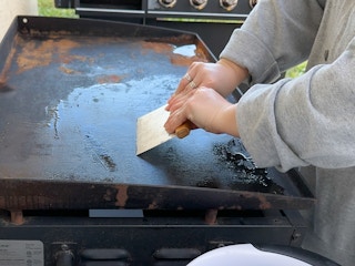 Someone scraping food debris off of a Blackstone griddle