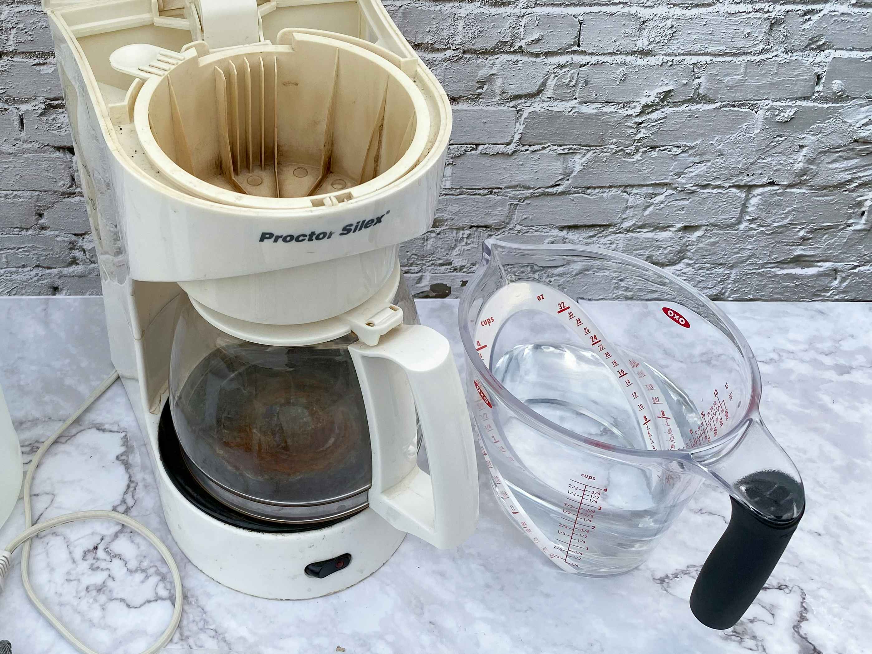 A coffee maker in need of cleaning on a counter next to a measuring cup of a water and vinegar mixture