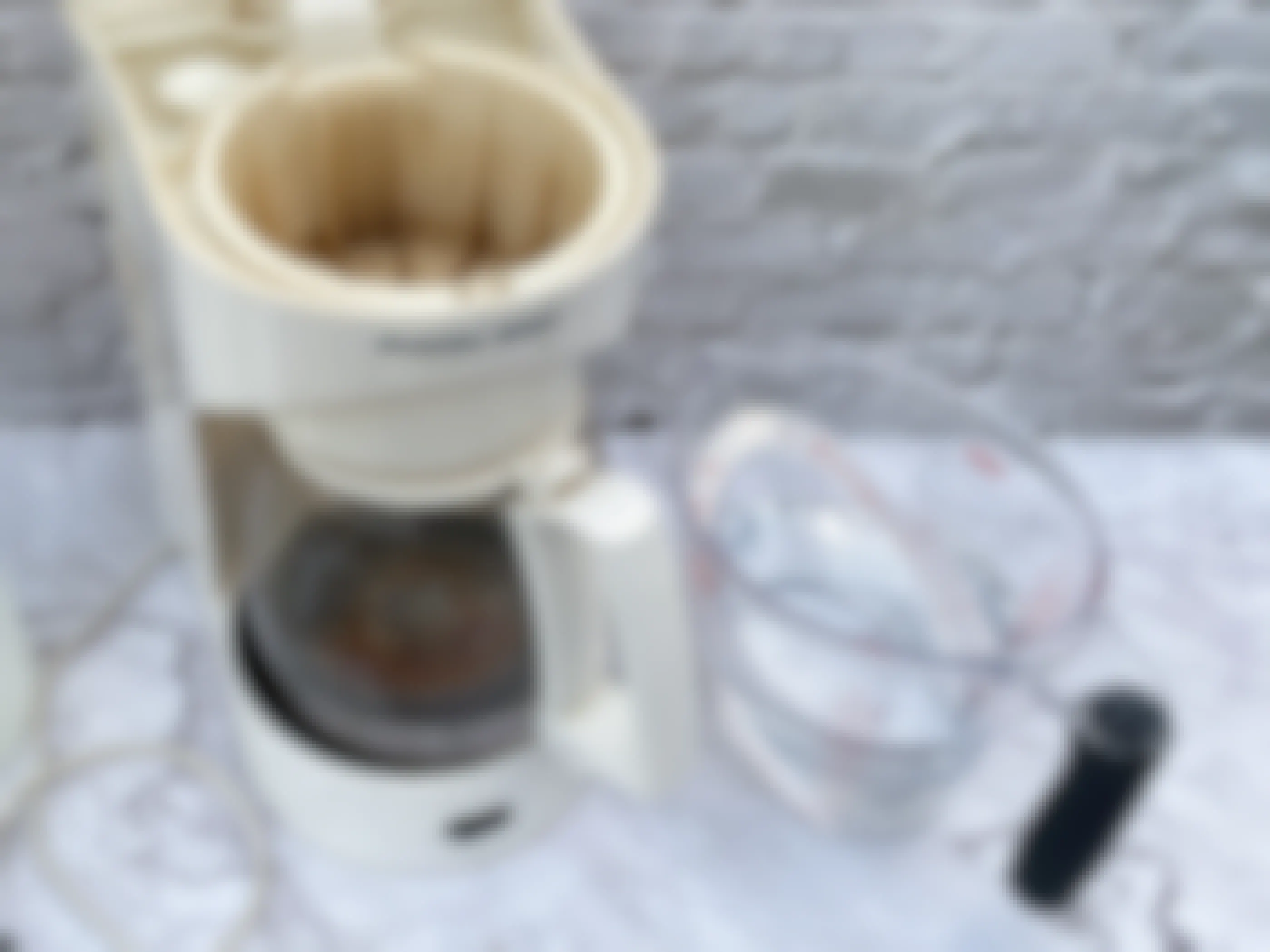 A coffee maker in need of cleaning on a counter next to a measuring cup of a water and vinegar mixture