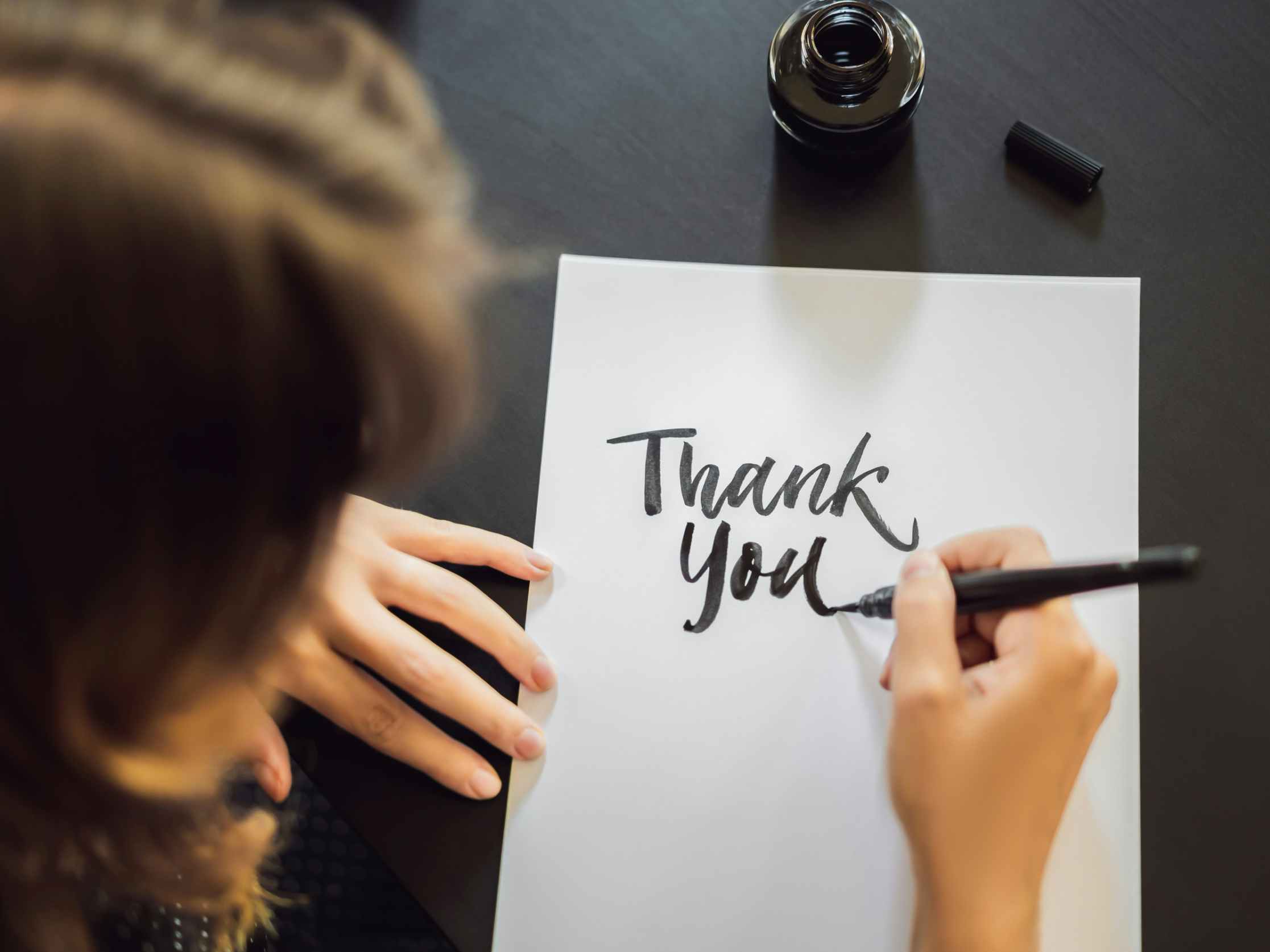 Someone writing "thank you" on a piece of paper in calligraphy