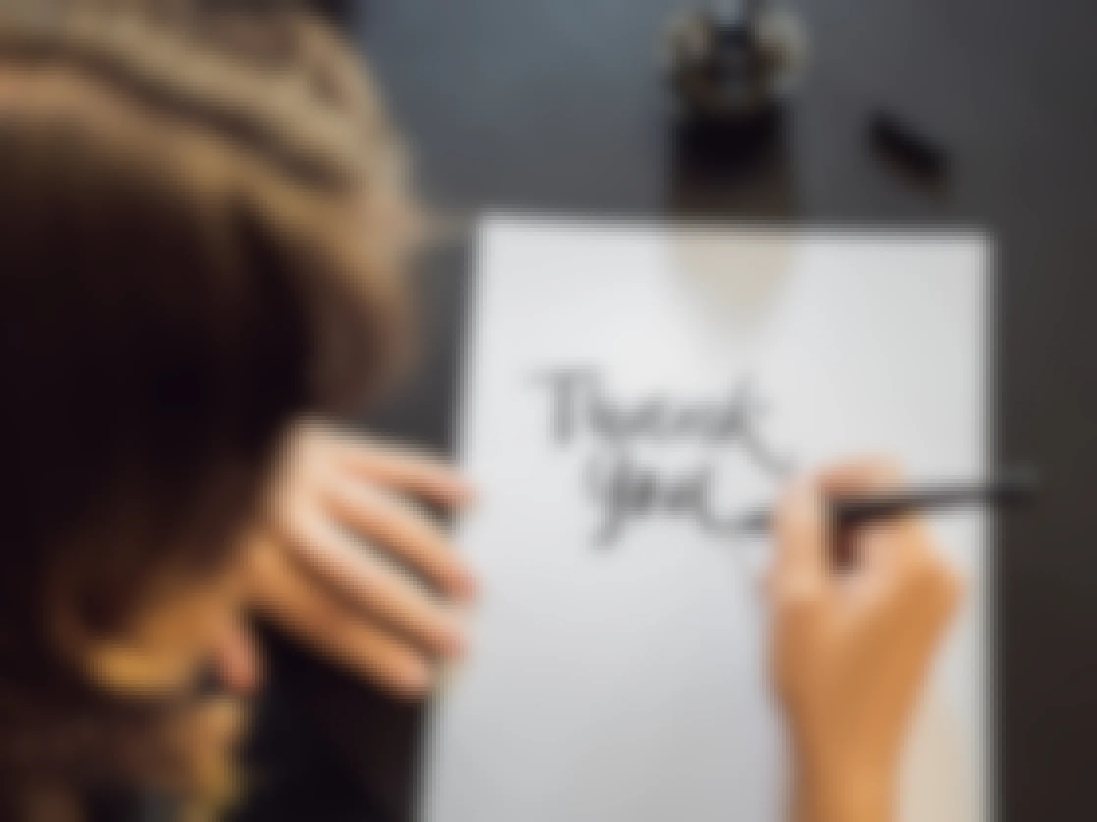 Someone writing "thank you" on a piece of paper in calligraphy