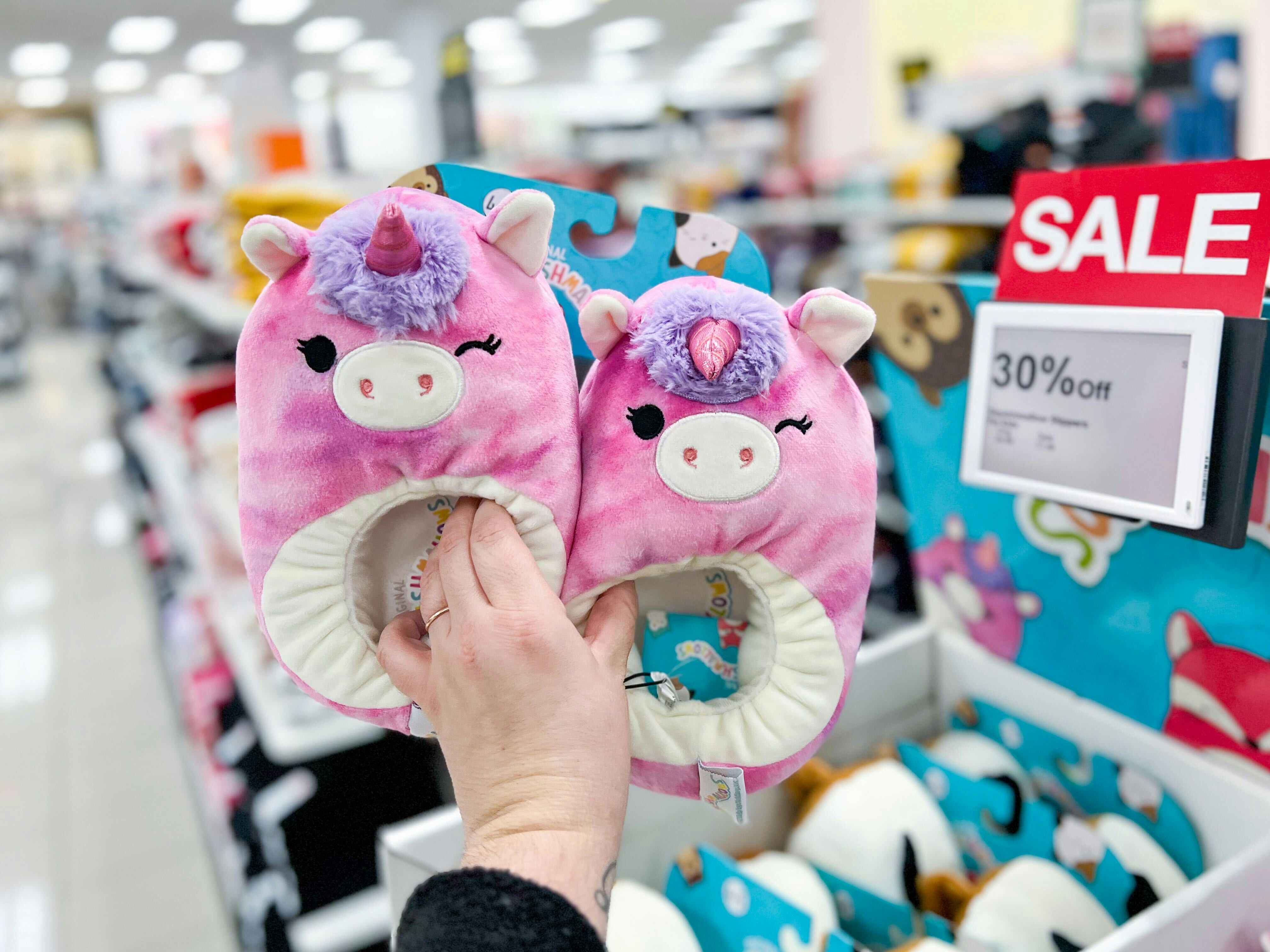 person holding squishmallow slippers in front of kohls sale sign