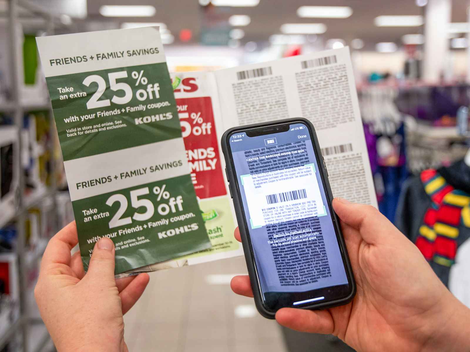 a person holding kohls coupons while scanning barcode on cellphone in store 