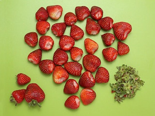 cut strawberries on green cutting board with stems removed