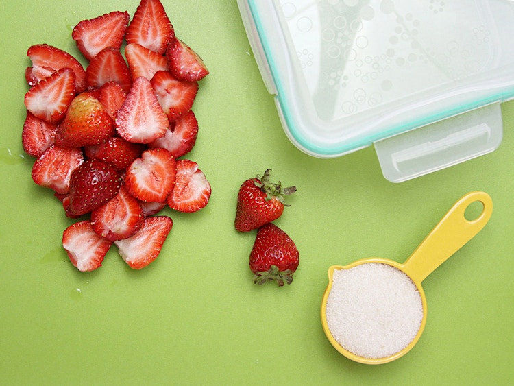 sliced strawberries with measuring cup full of sugar for storing