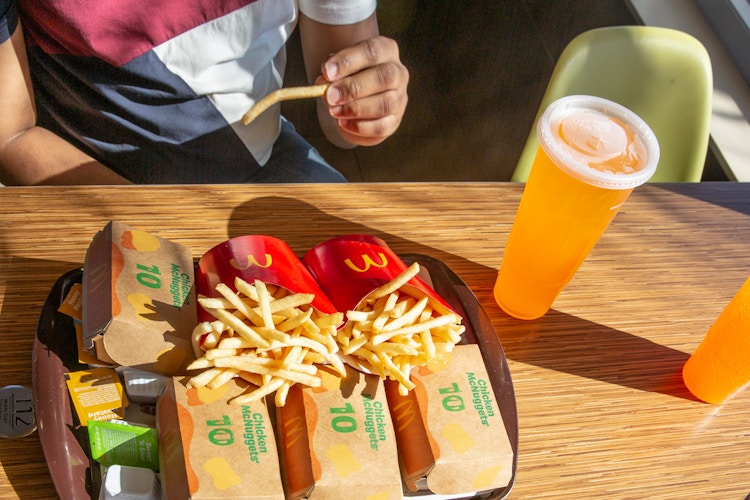 Person sitting down at a mcdonalds restuarant eating the 40 piece chicken nugget meal with two large fries and drinks